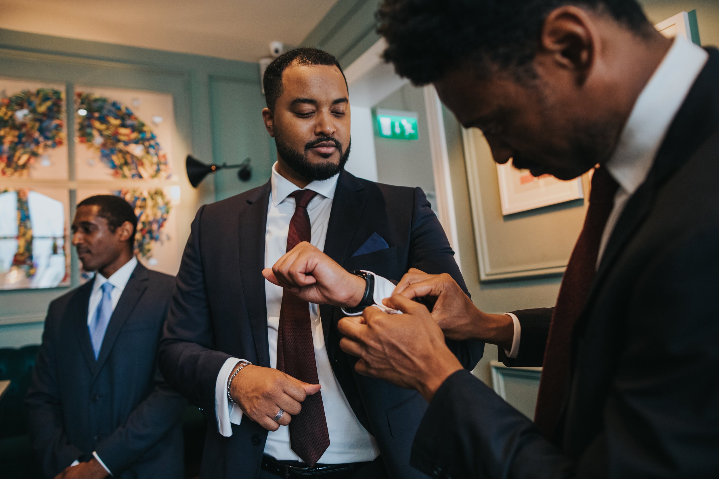 Groomsmen help one and other with cufflinks