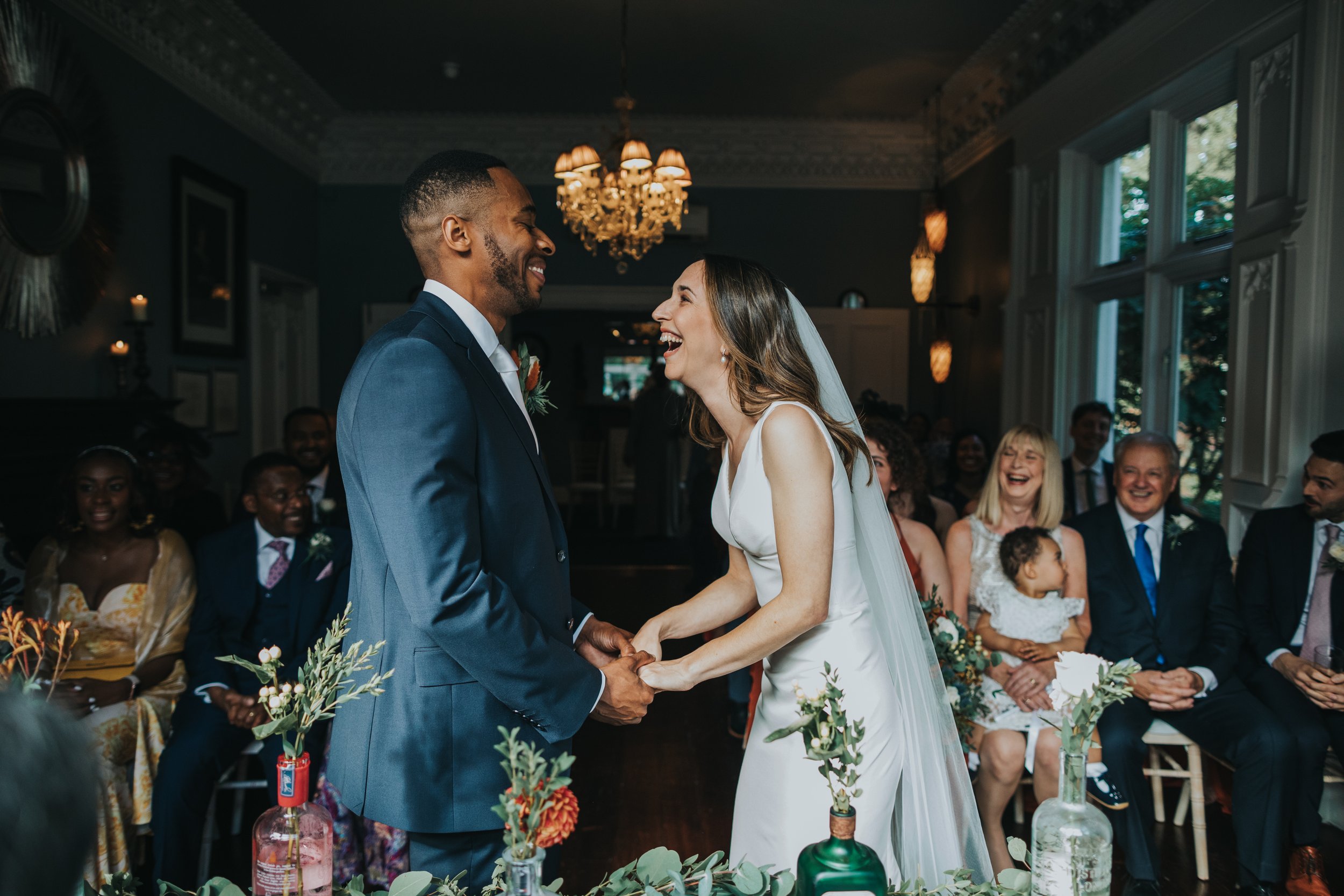 Bride and Groom laugh together holding hands during their wedding ceremony at Didsbury House.