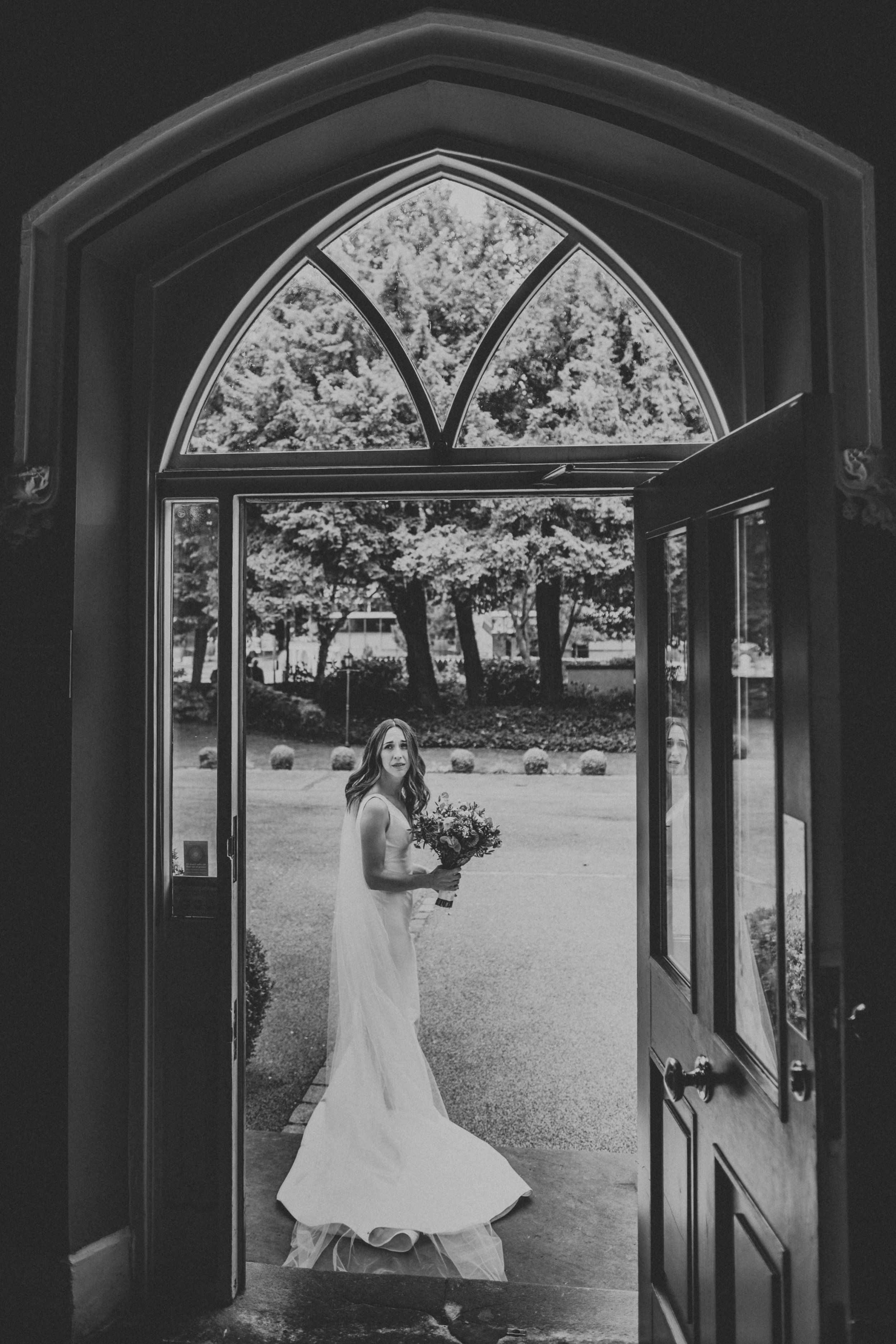Bride standing in door way waiting for groom at Didsbury House. Photo in black at white. 