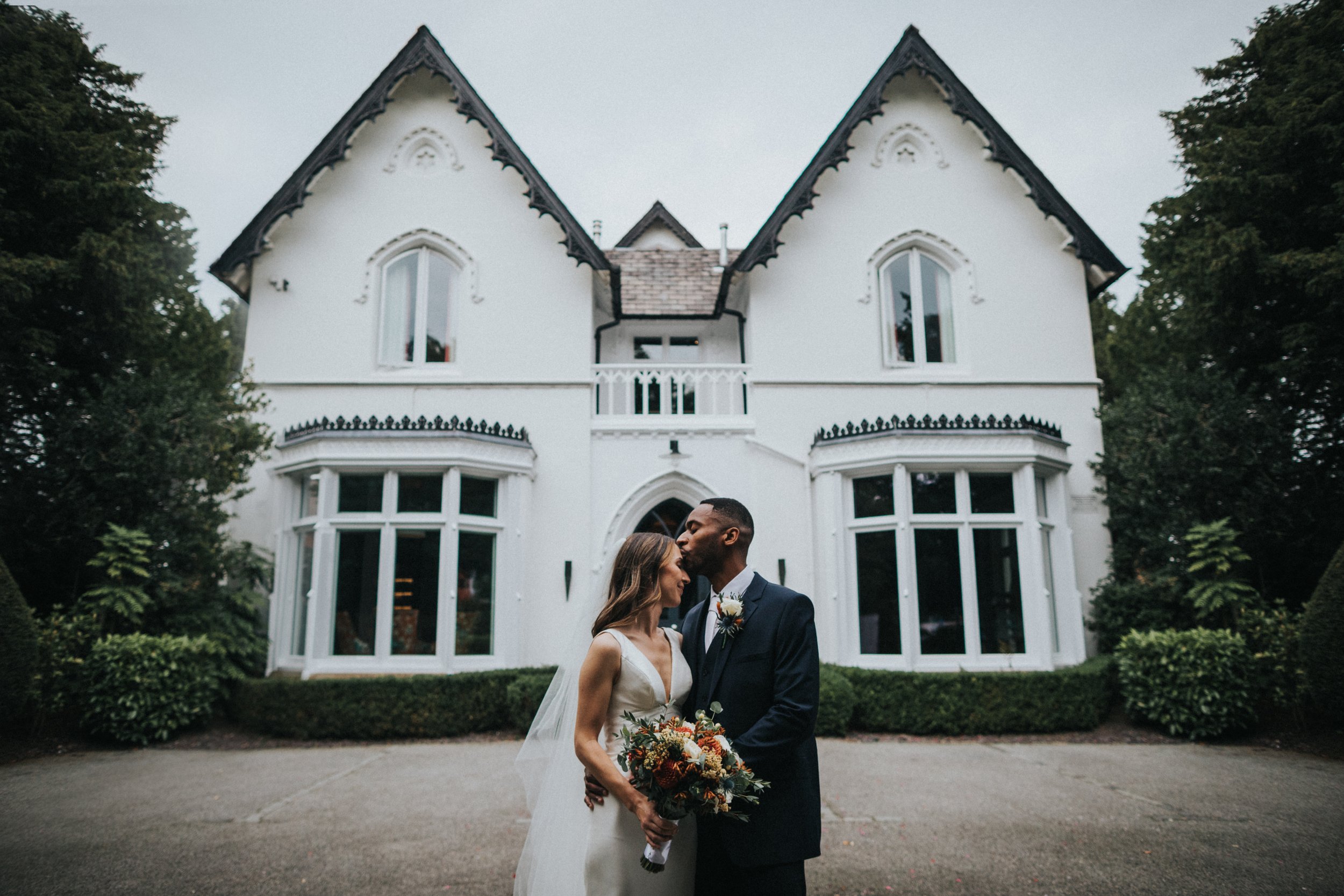 Groom kisses bride on the head in front of Didsbury House Hotel.