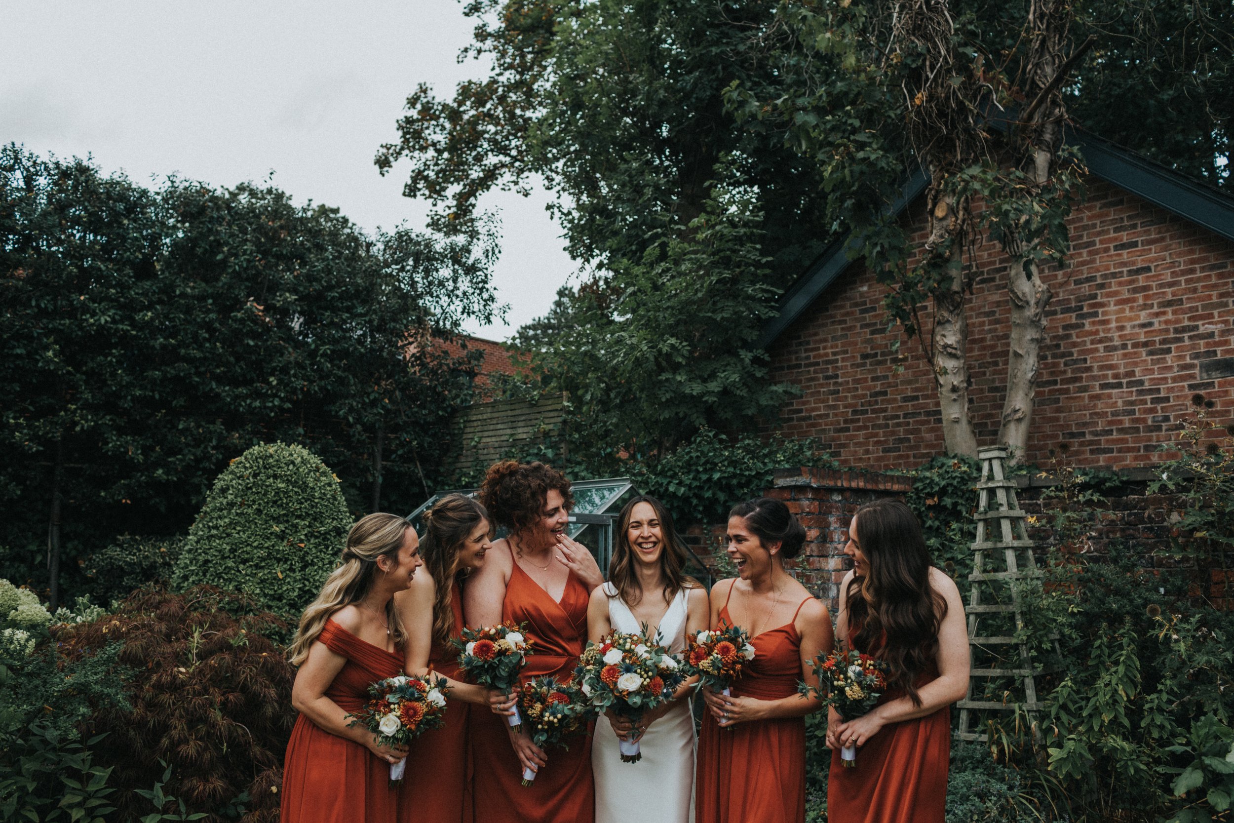 Bridesmaids laugh holding their flowers. 