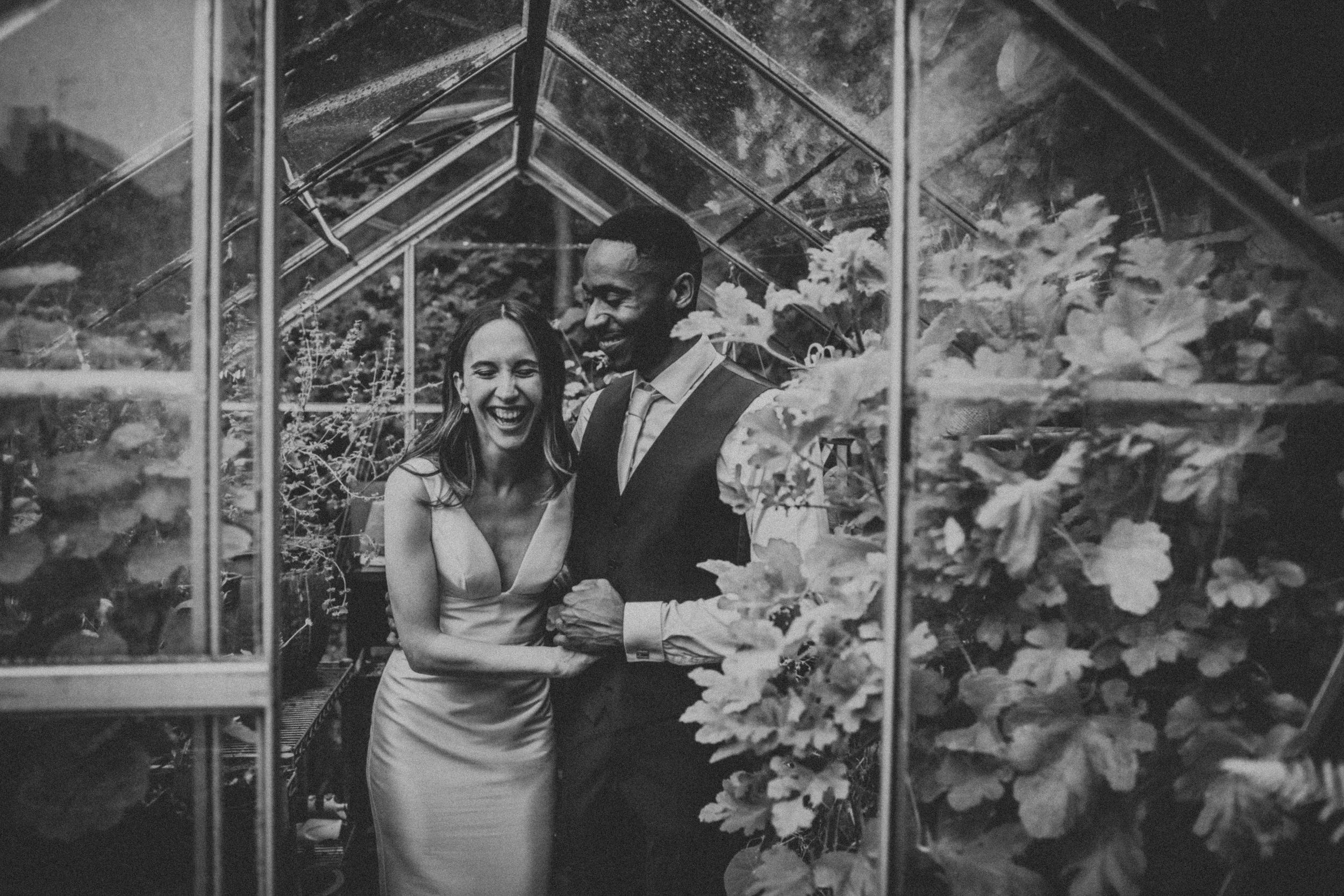 Black and white photo of Bride and Groom laughing together in greenhouse. 