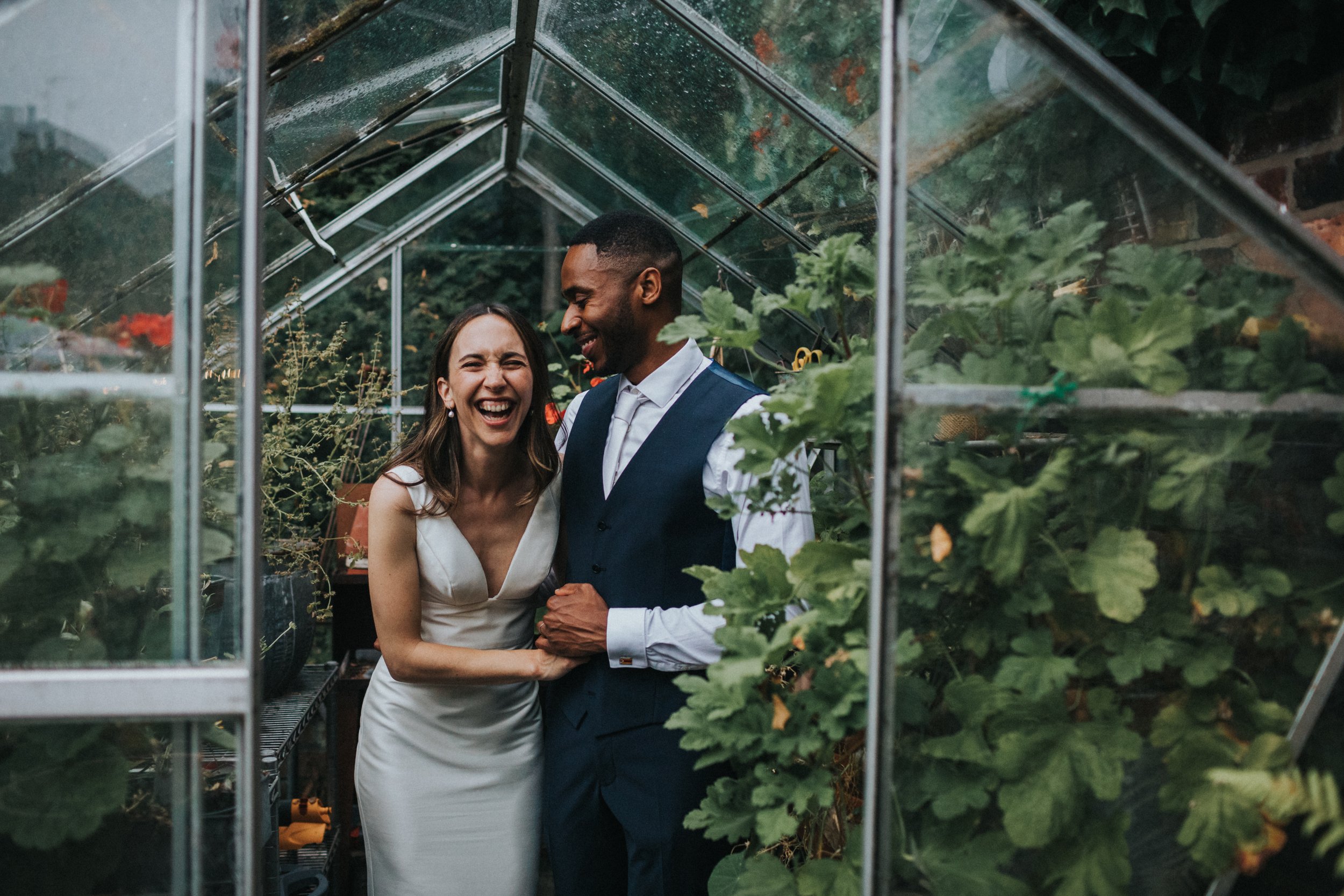 Bride and groom laughing in green house.