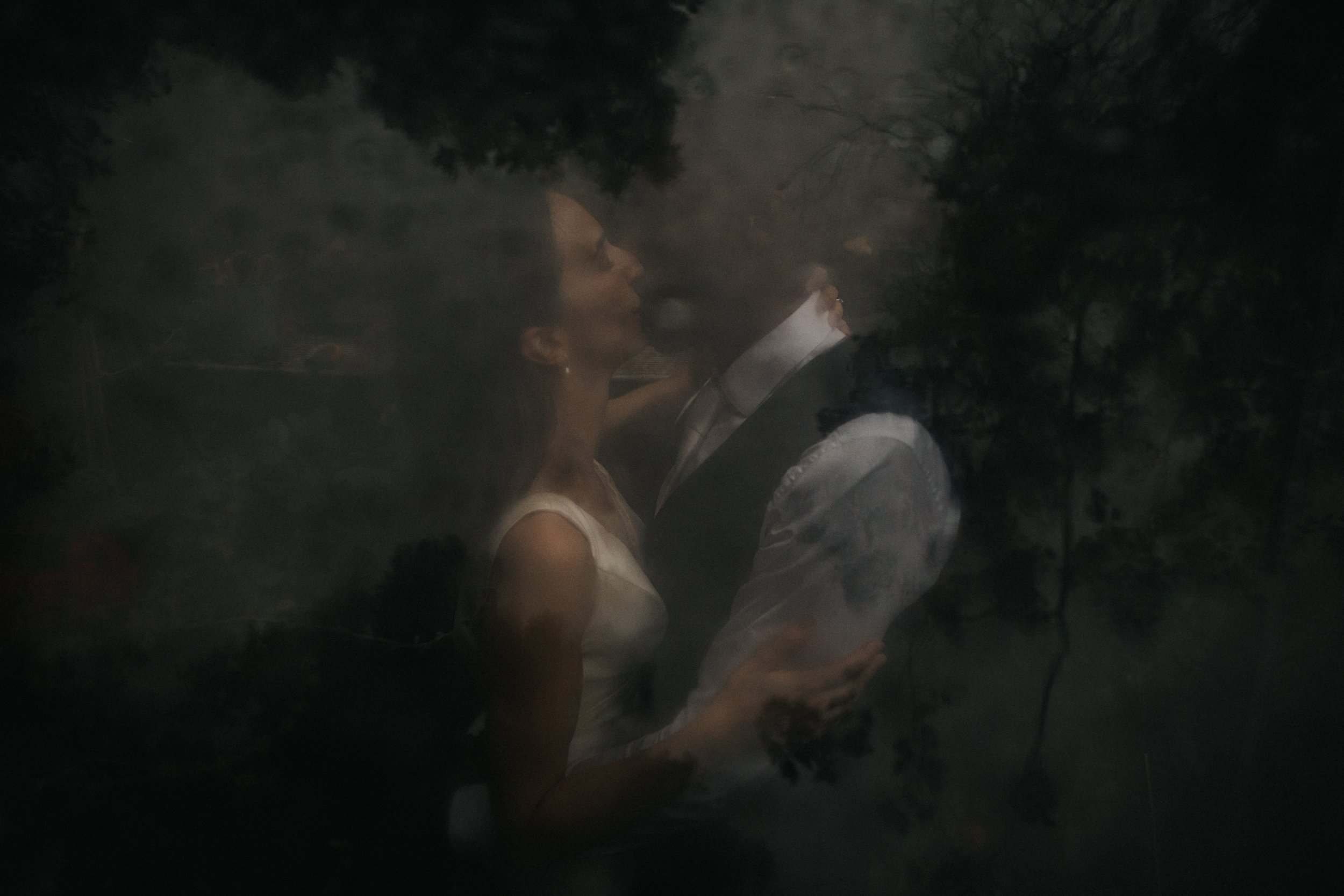 Dark photo of Bride and Groom kissing through greenhouse glass. 