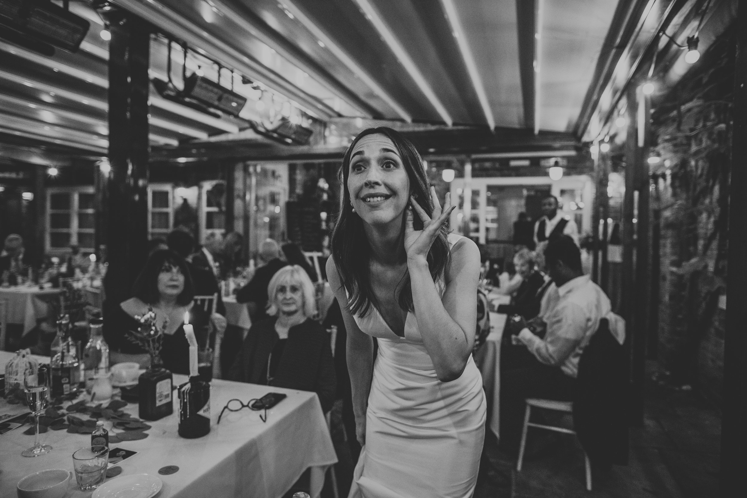 Black and white photo of Bride holding her ear as if to listen to someone. 