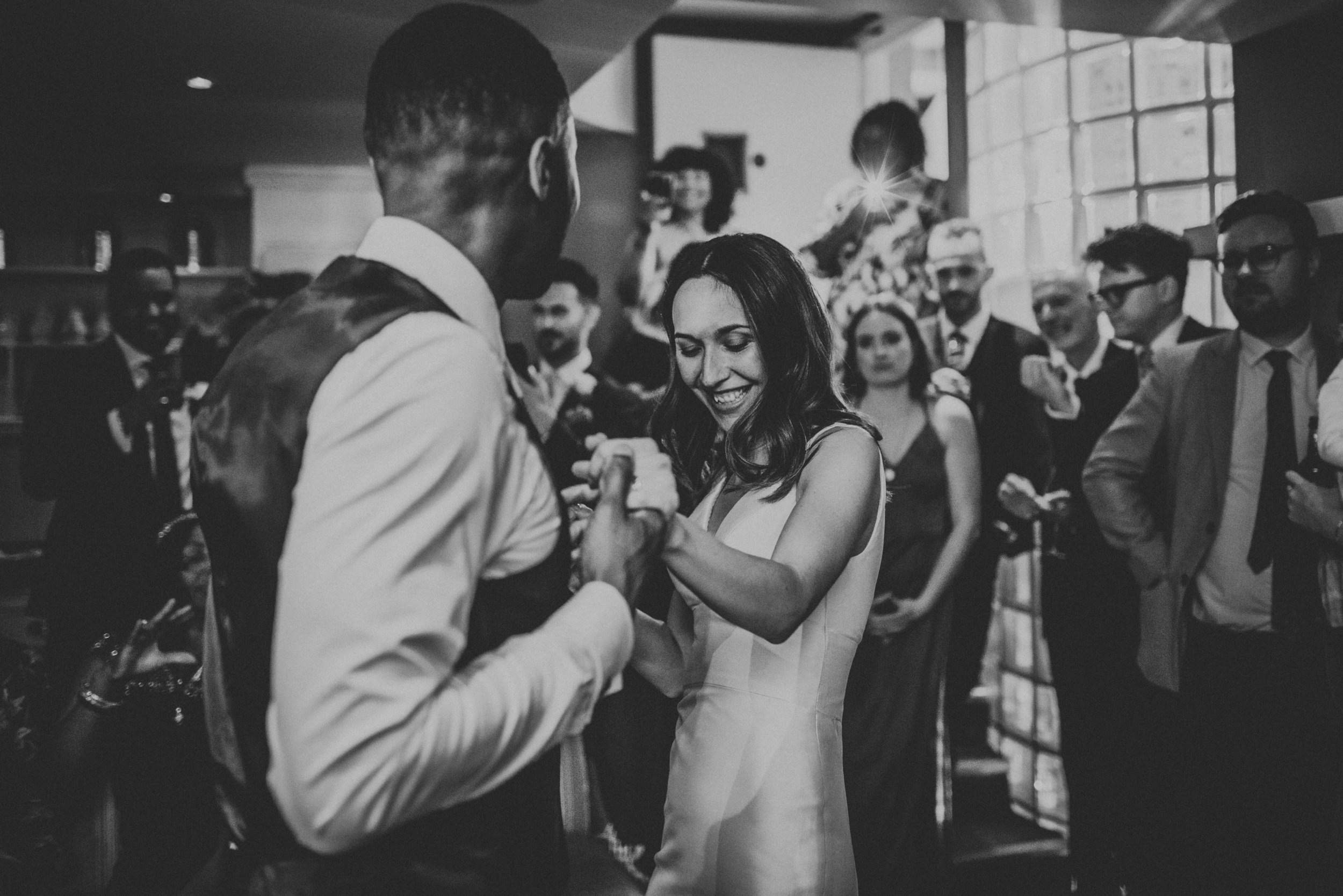 Bride smiling and dancing with her husband as guests take photos in the back ground. 