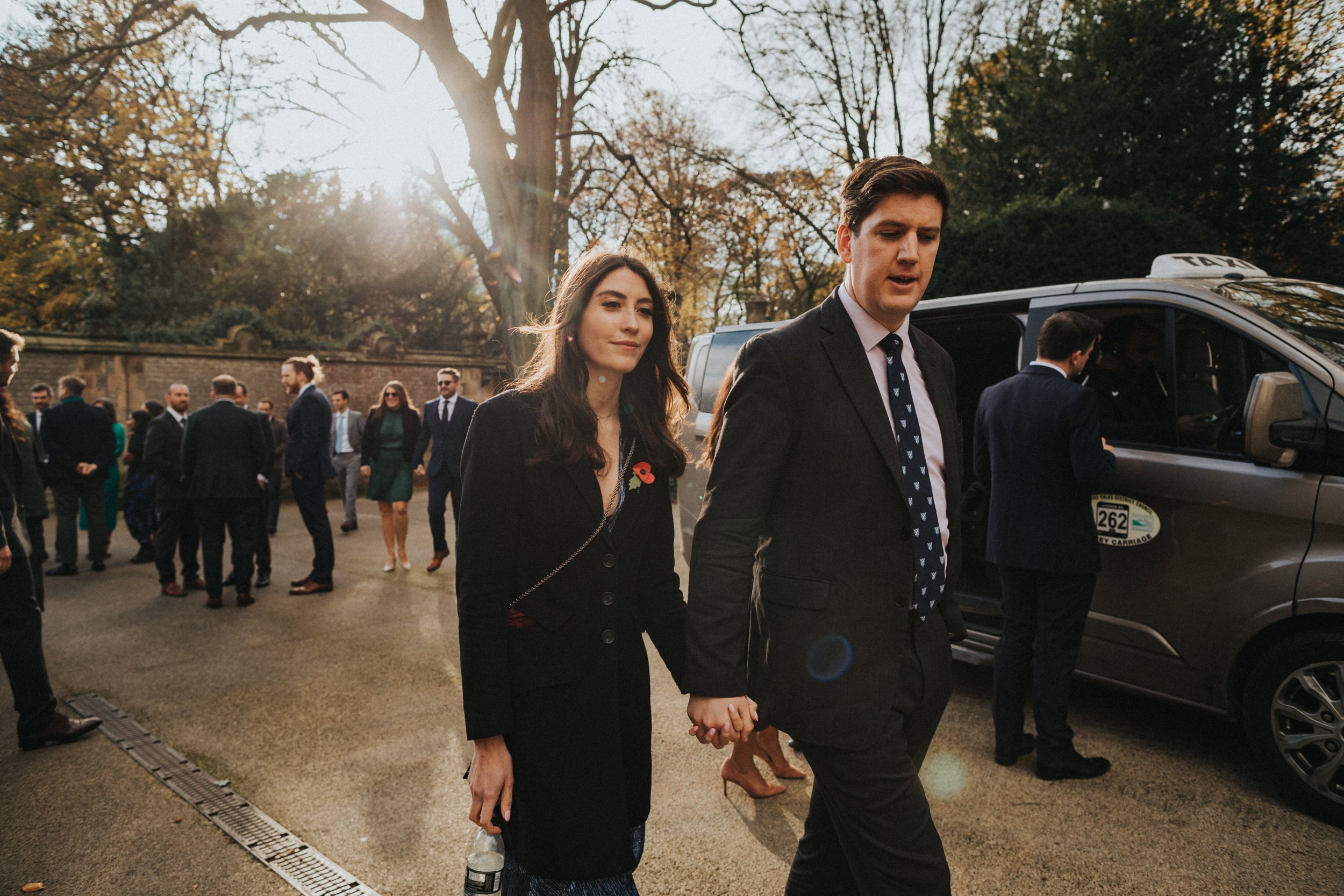 Wedding guests arrive on foot back lit by the winter sun. 