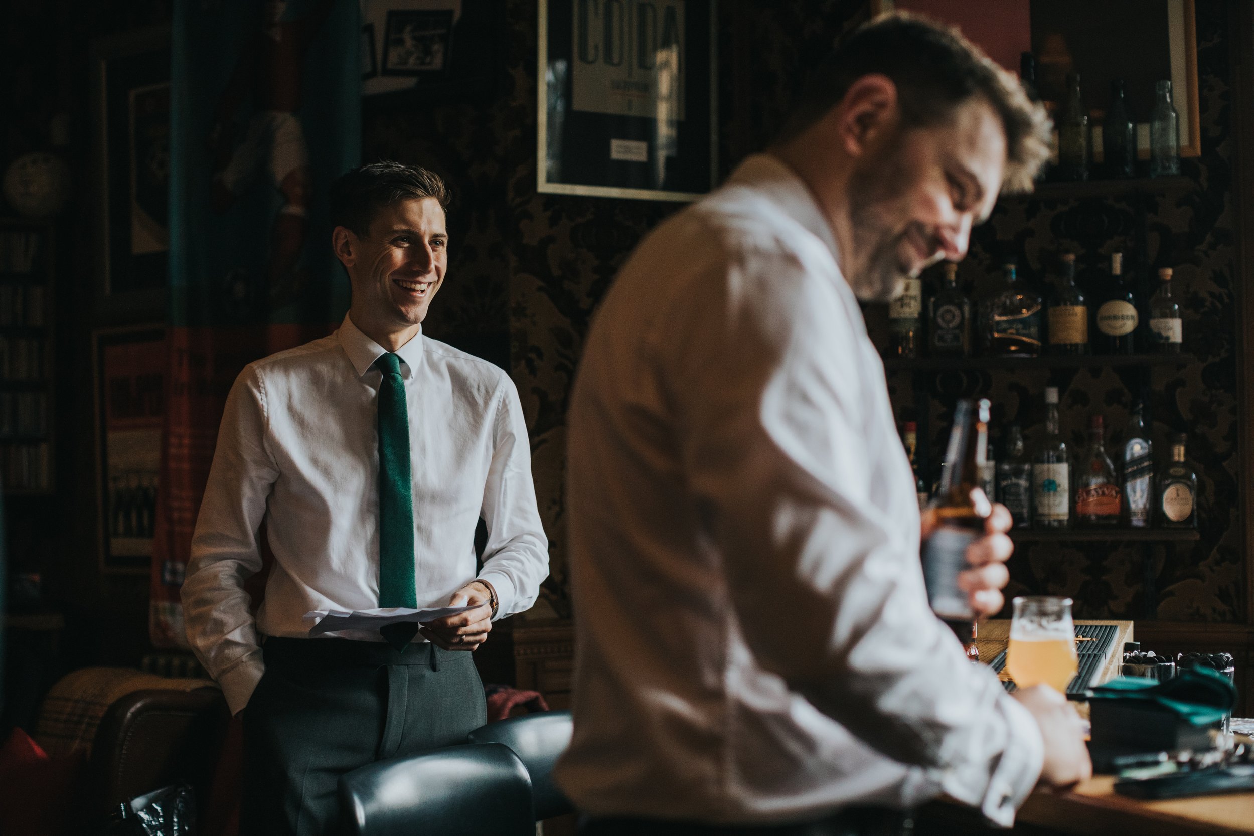 Groomsmen enjoy the sunlight steaming through the windows while sipping on a beer. 