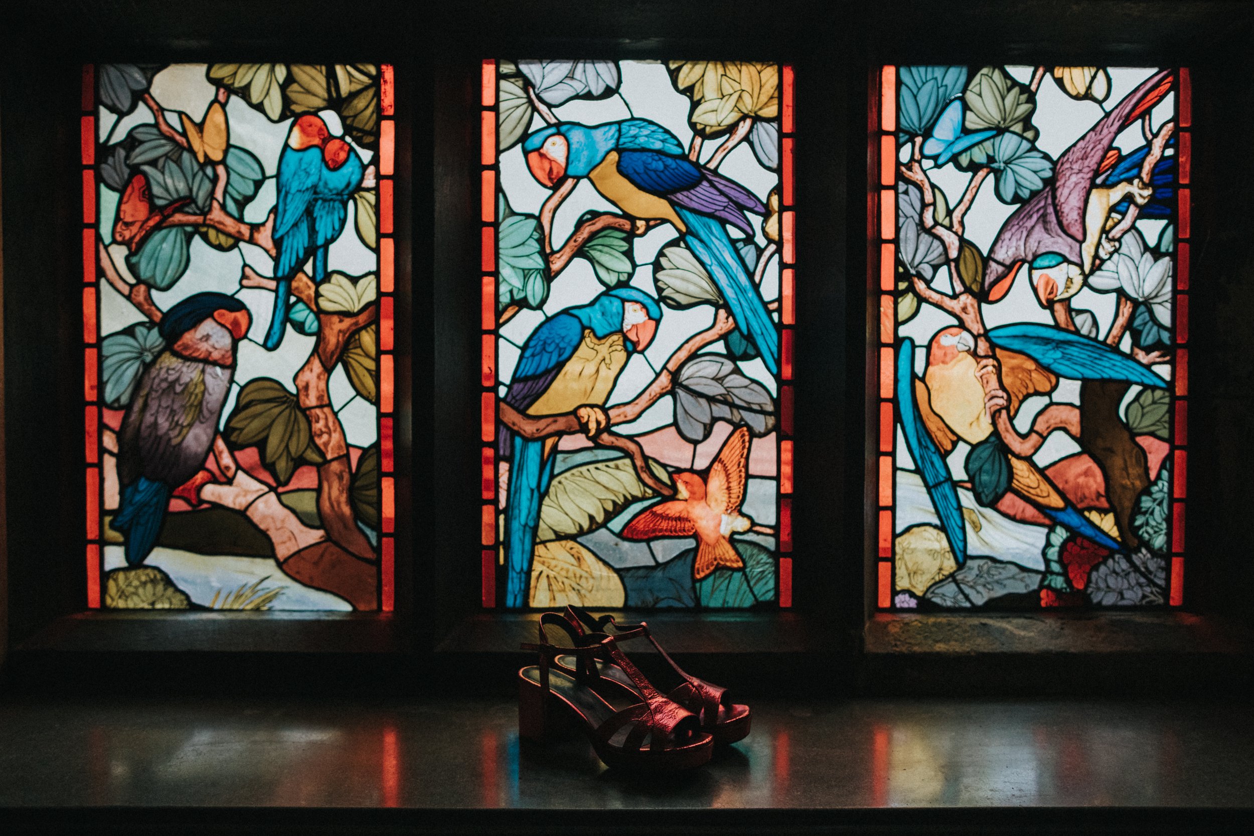 Brides red shoes sit in front of a stained glass window. 