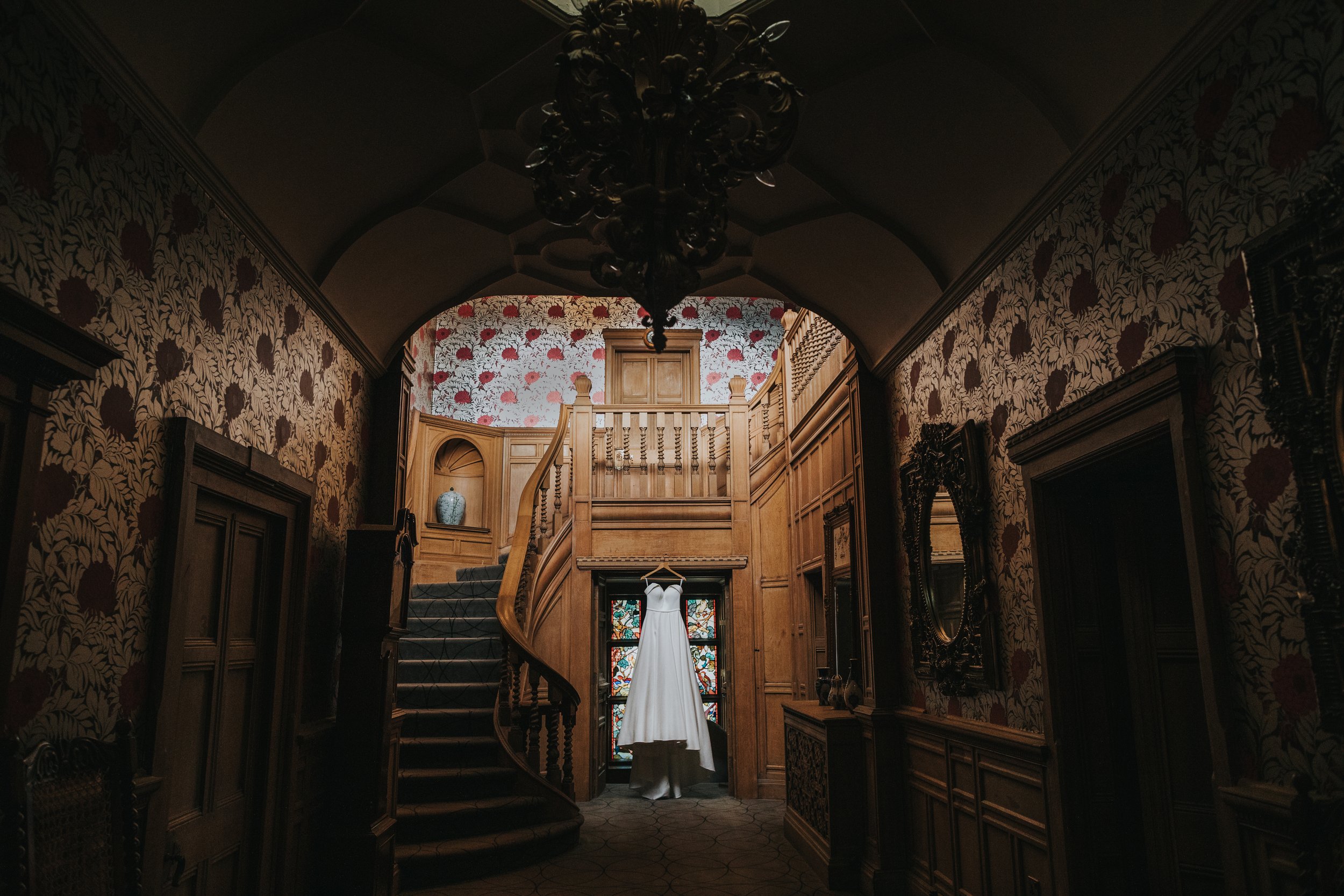 The wedding dress hangs in the hallway of Thornbridge Hall in front of a colourful stained glass window. 