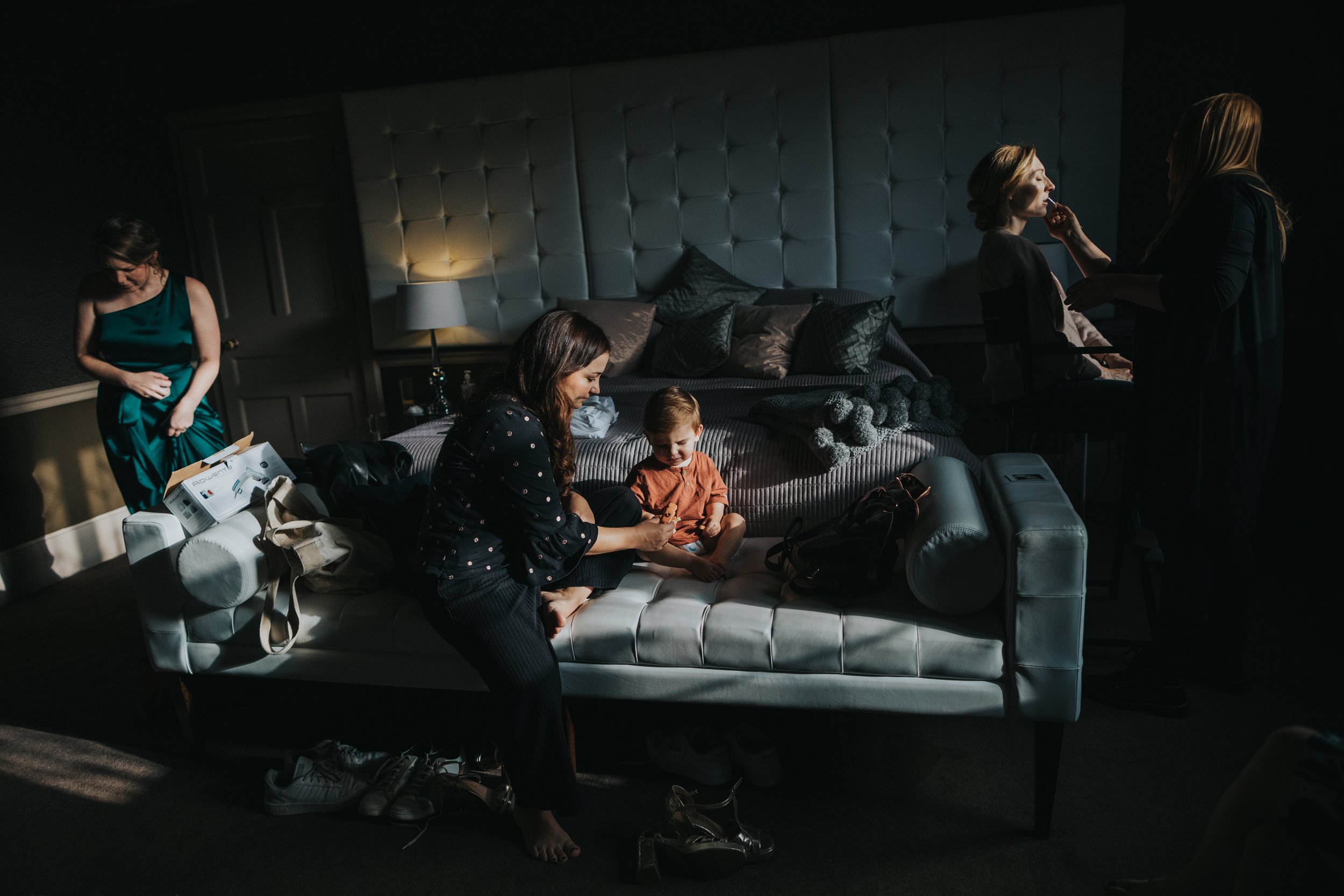 Mother gives her baby some treats at the foot of the bed as the bridesmaids get ready around her. 