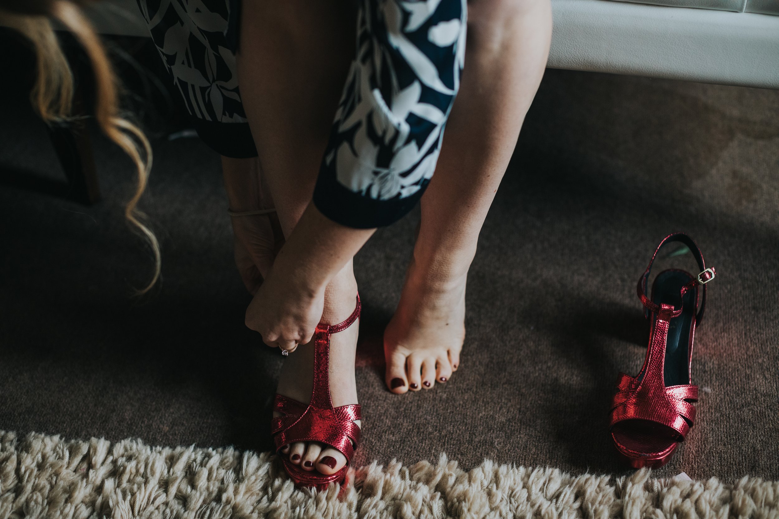 Bride puts of her red wedding shoes. 