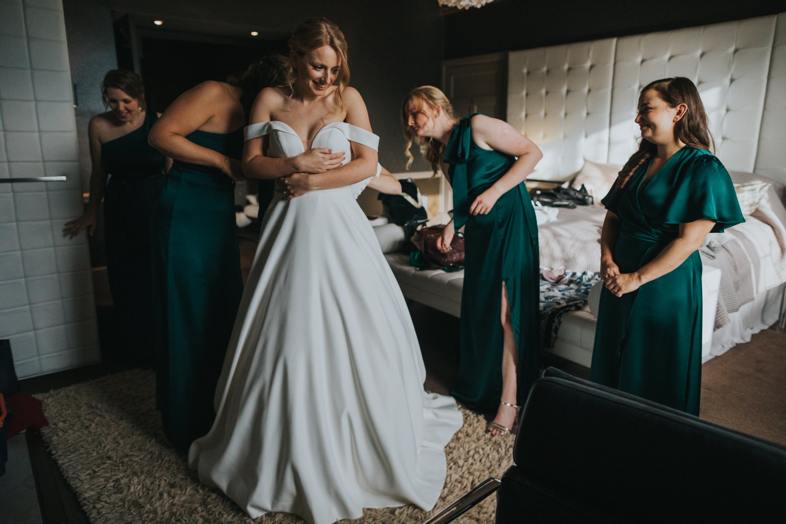 Bridesmaids help bride into her dress. 