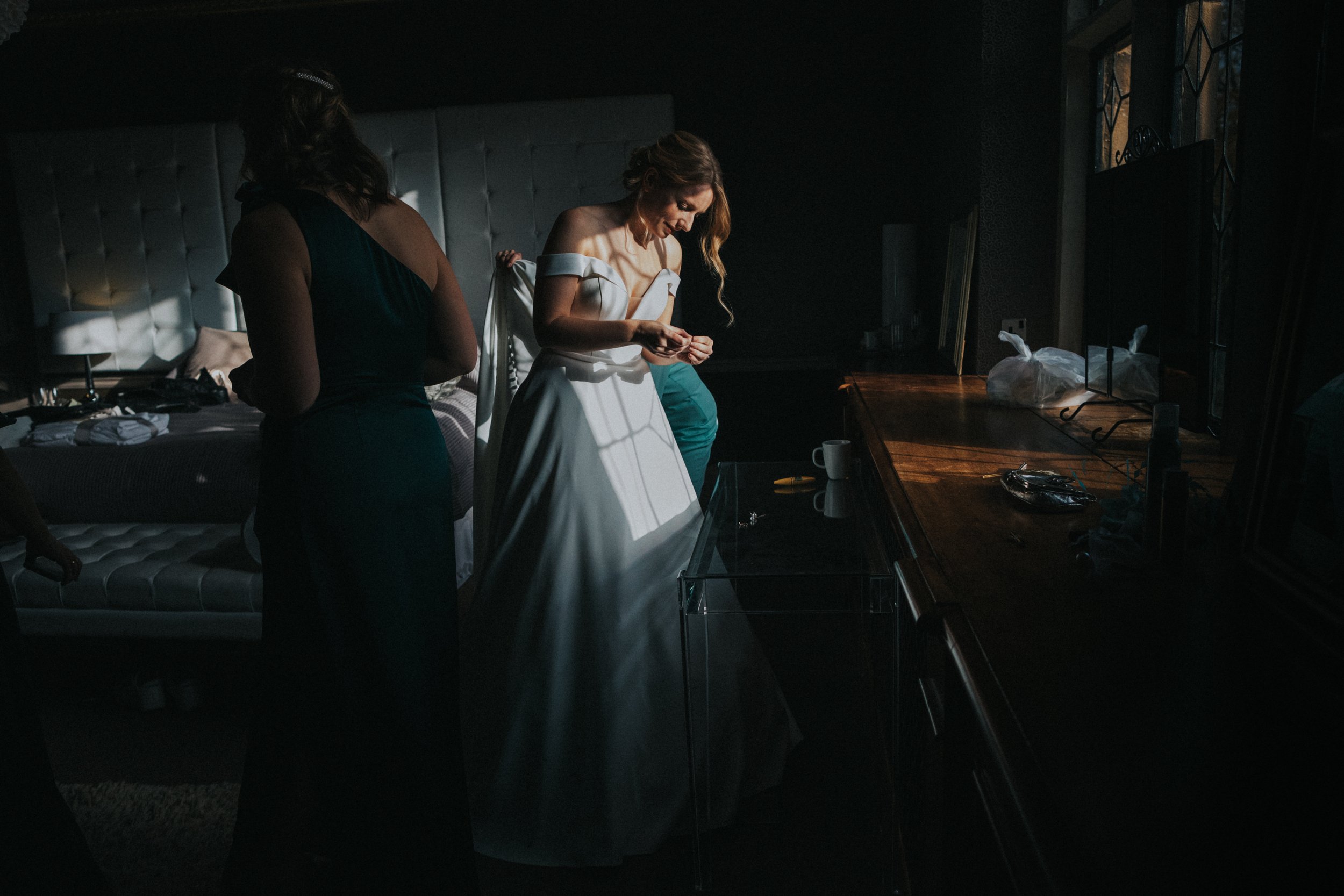 Bride stands in the window light while putting on her earrings. 