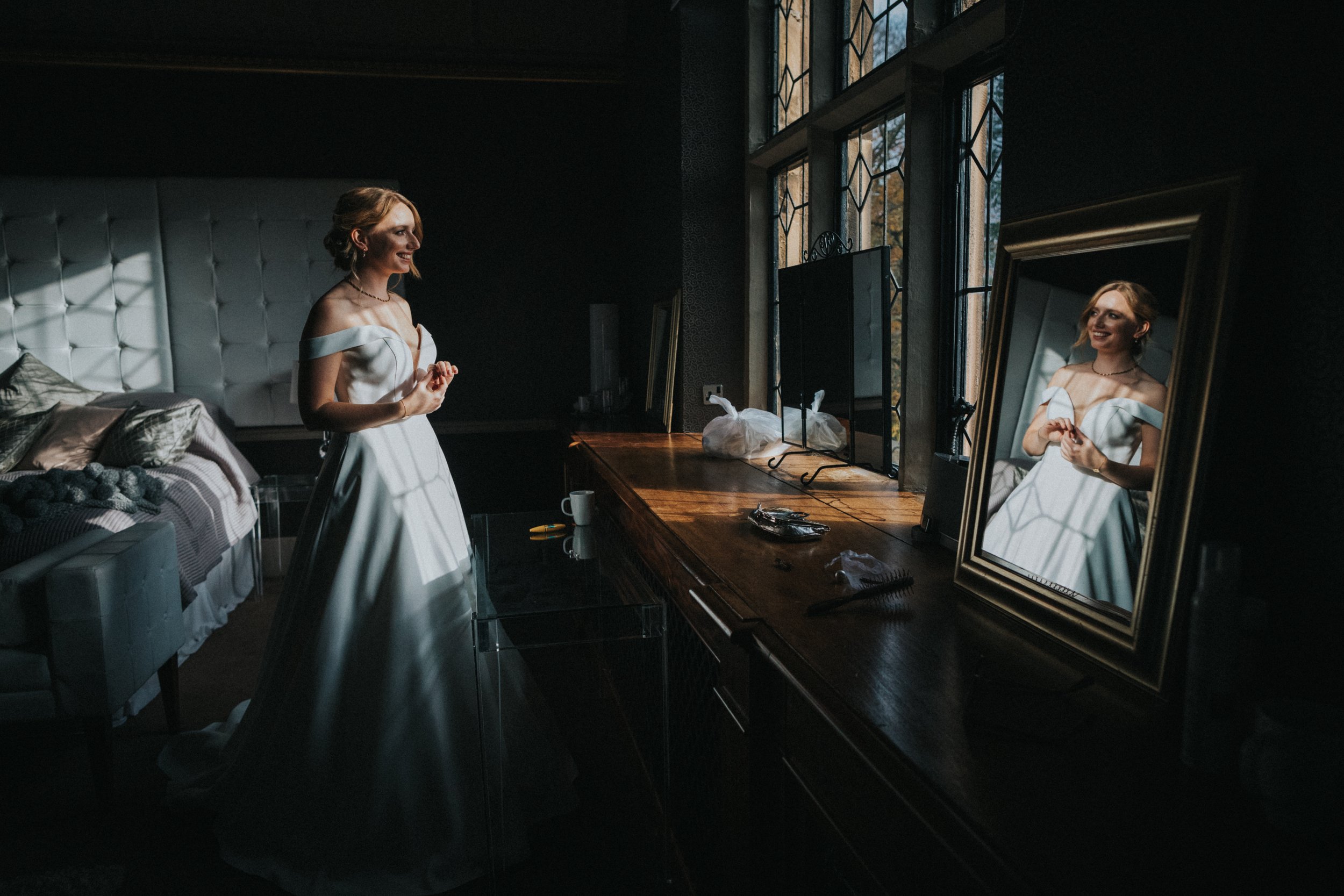 Bride stands in the window light and is reflected in the mirror. 