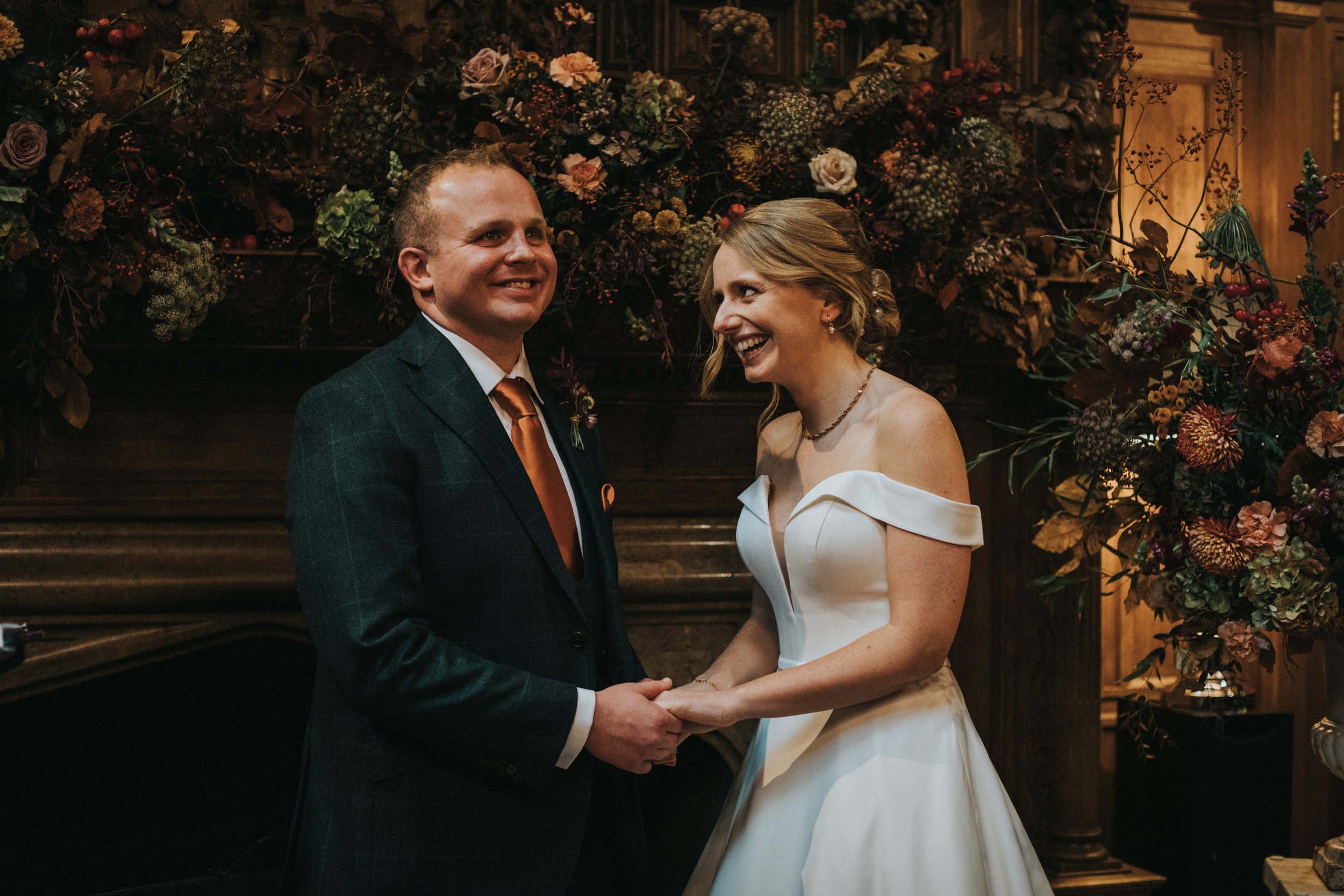 Bride and Groom hold hands facing on and other and laughing during the ceremony. 