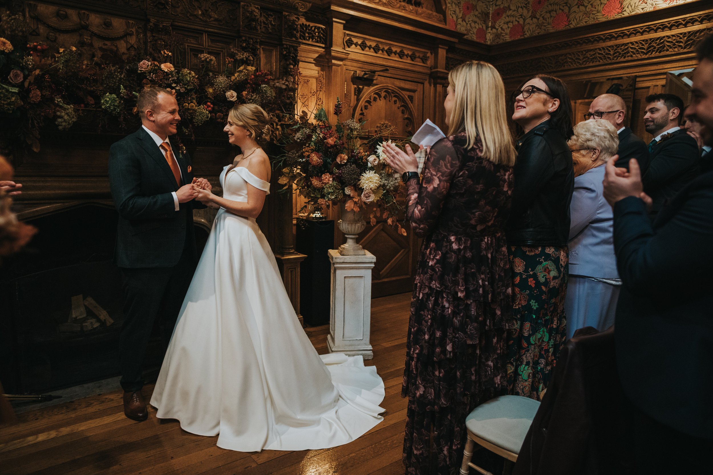 Bride and Groom stand and look at one and other laughing as guests stand an applause. 