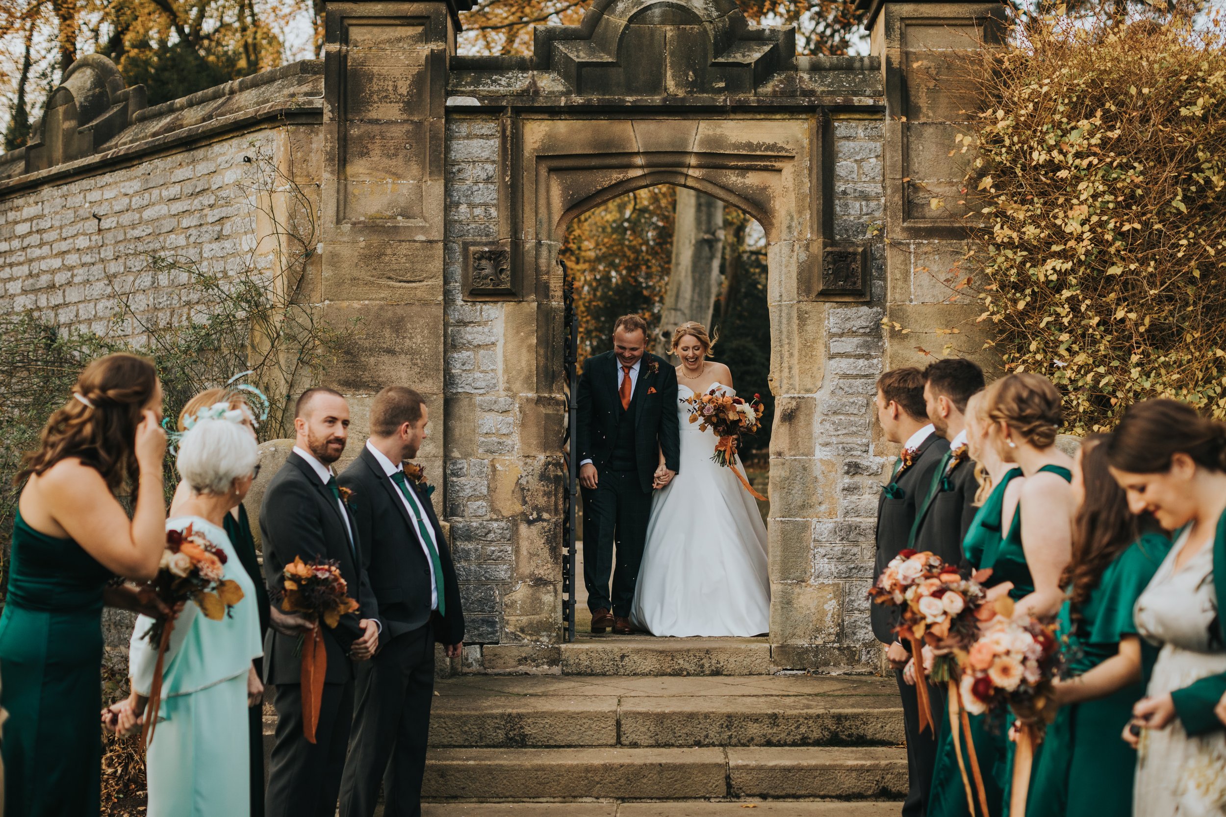 Bride and groom walk through the stone arched doorway in the garden at Thornbridge Hall 