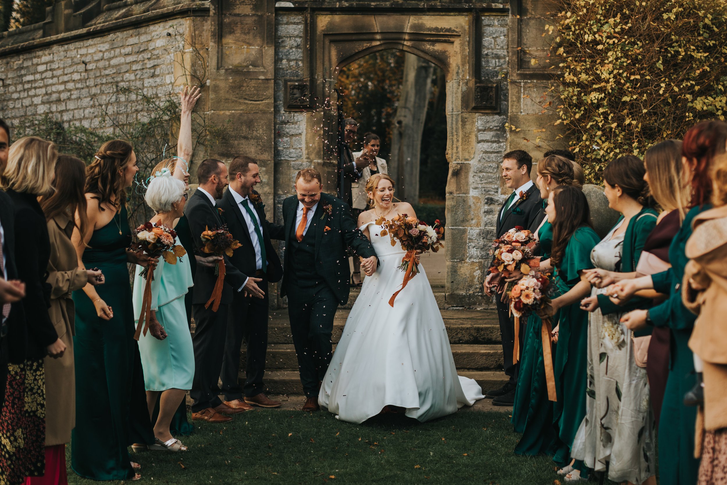 Bride and groom laugh as guests throw confetti at them 