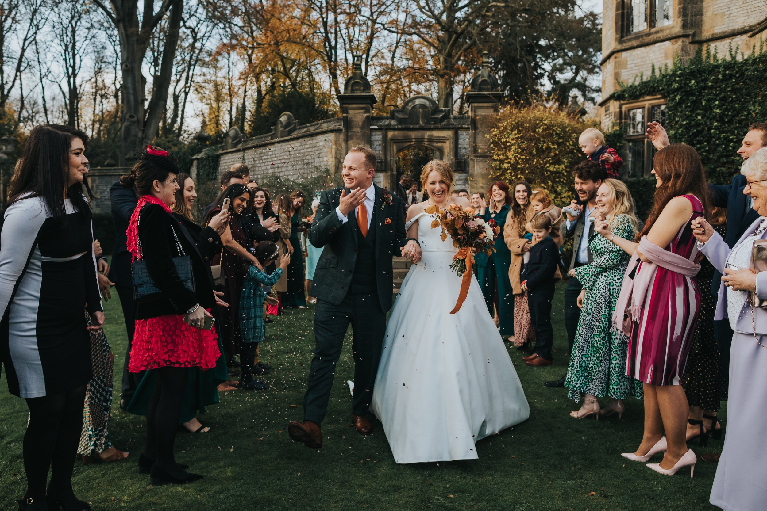 Groom wipes confetti from his face while Bride laughs. 