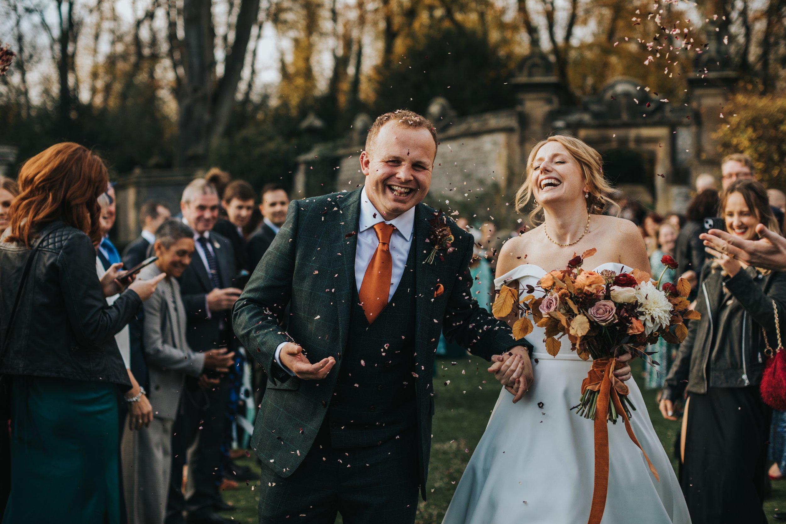 Groom looks at camera laughing as confetti is till being thrown at them. 