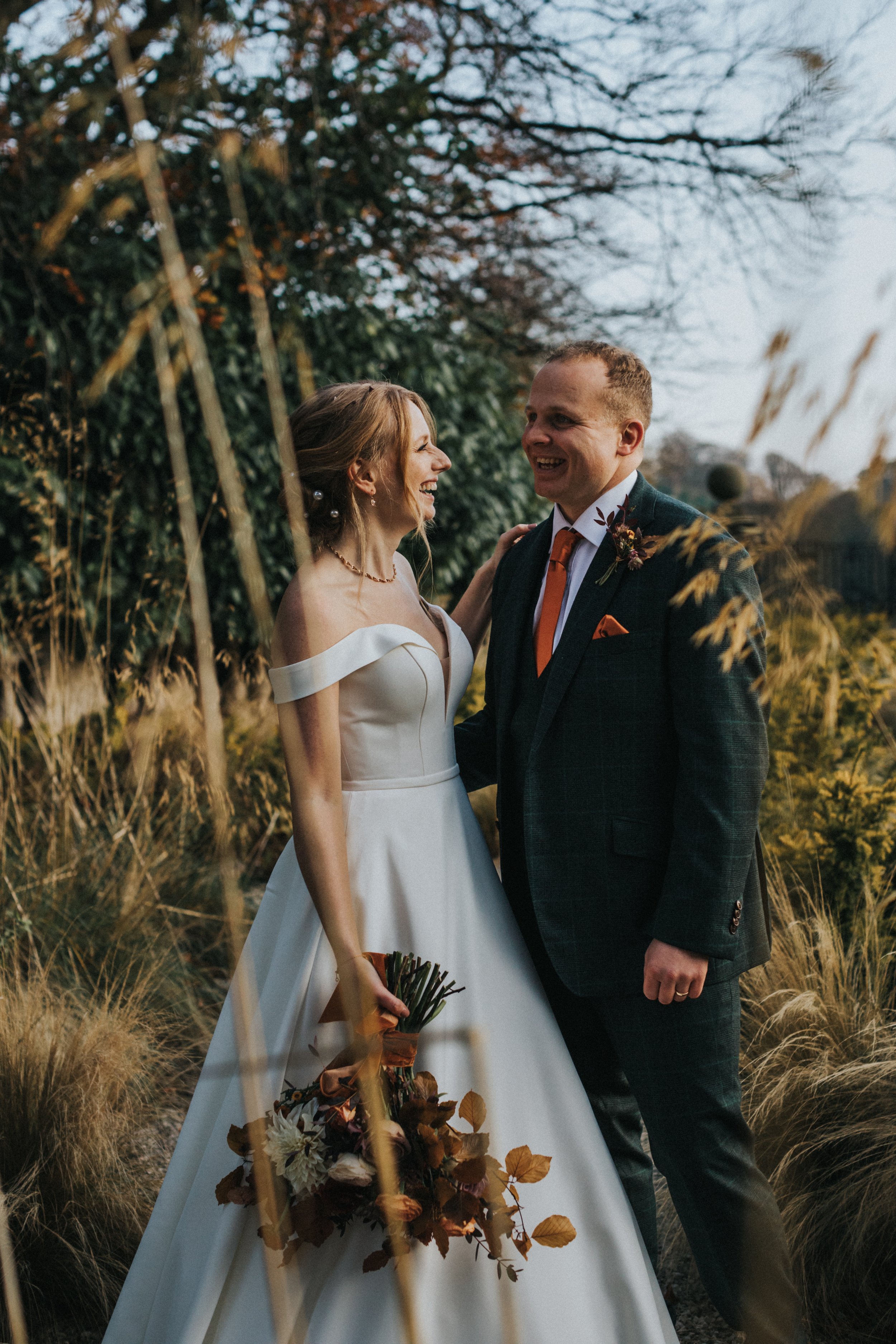 Bride and Groom stand together laughing in the long grassed gardens at Thornbridge Hall. 