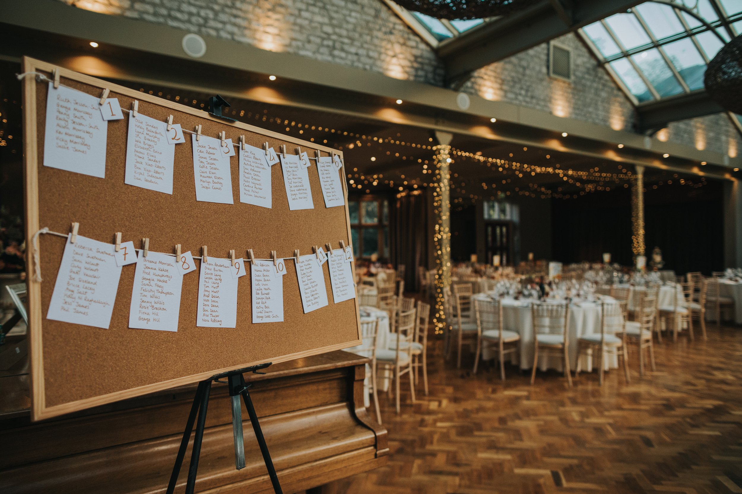 The cork board table plan with twinkly lights and chairs behind. 