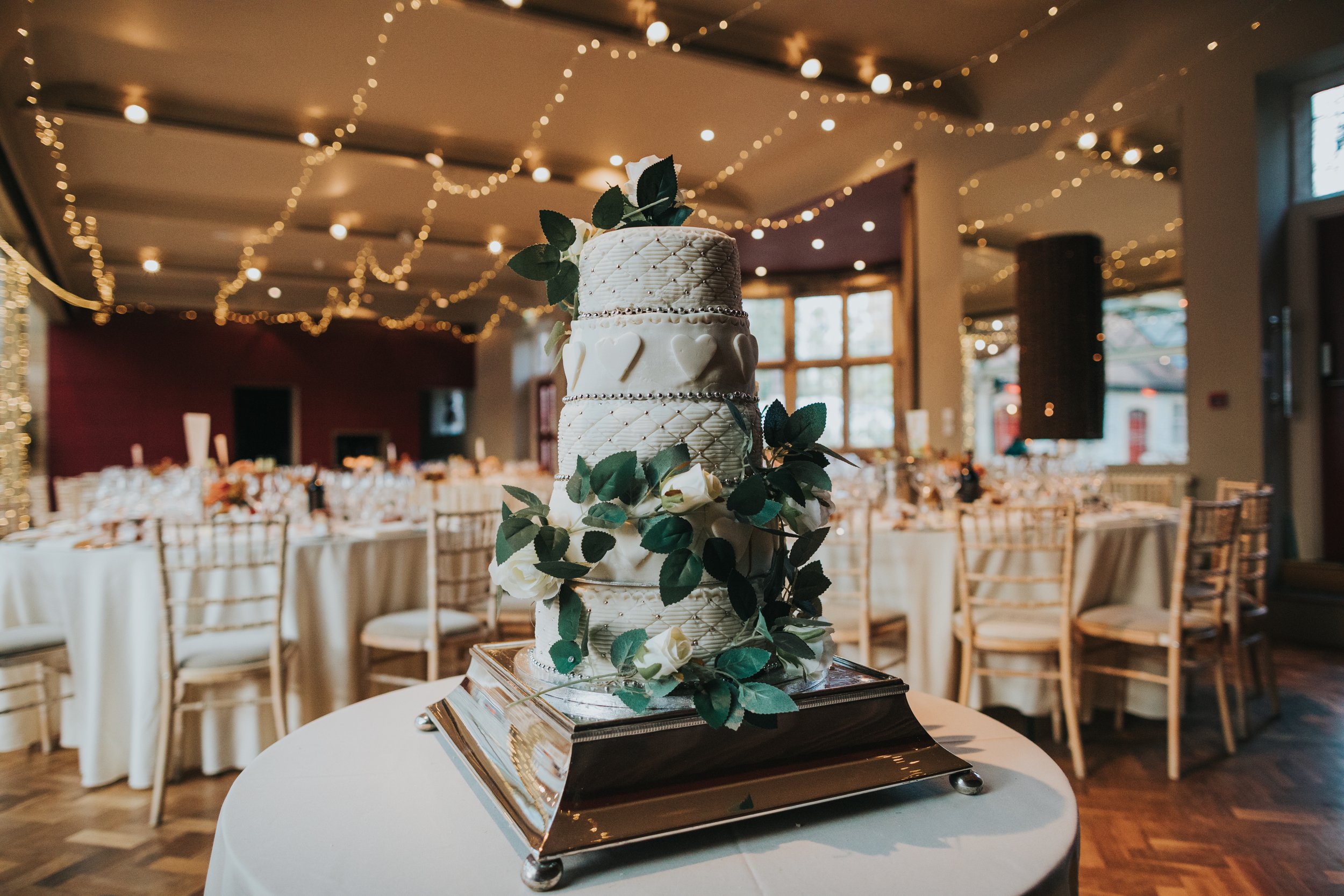 White wedding cake, with heart icing and twinkley lights behind it. 