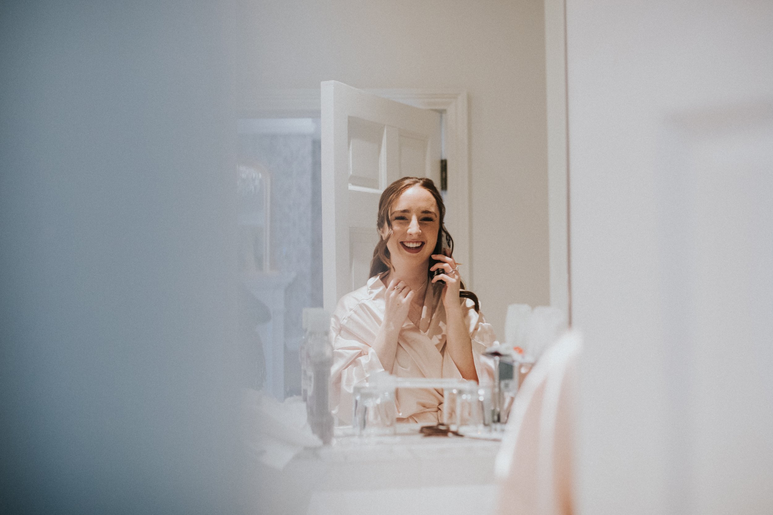 Bridesmaid reflected in the bathroom mirror and she talks on her mobile phone. 