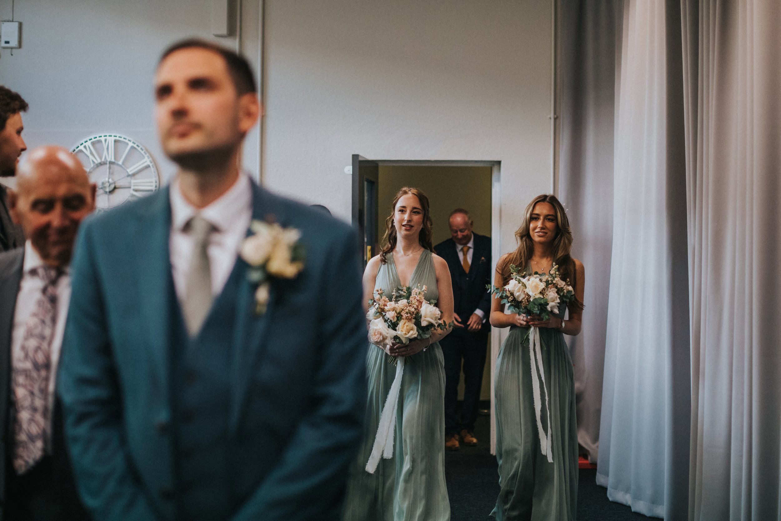 Bridesmaids walking down the aisle as groom looks emotional. 