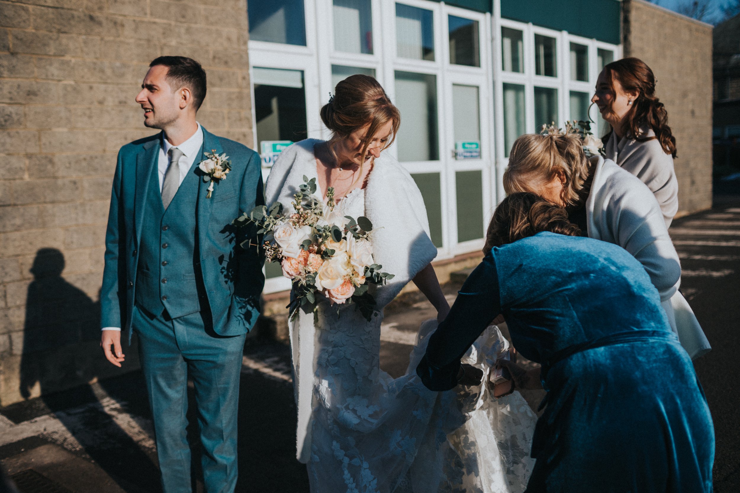 Mothers of the bride and groom help the bride with her dress. 