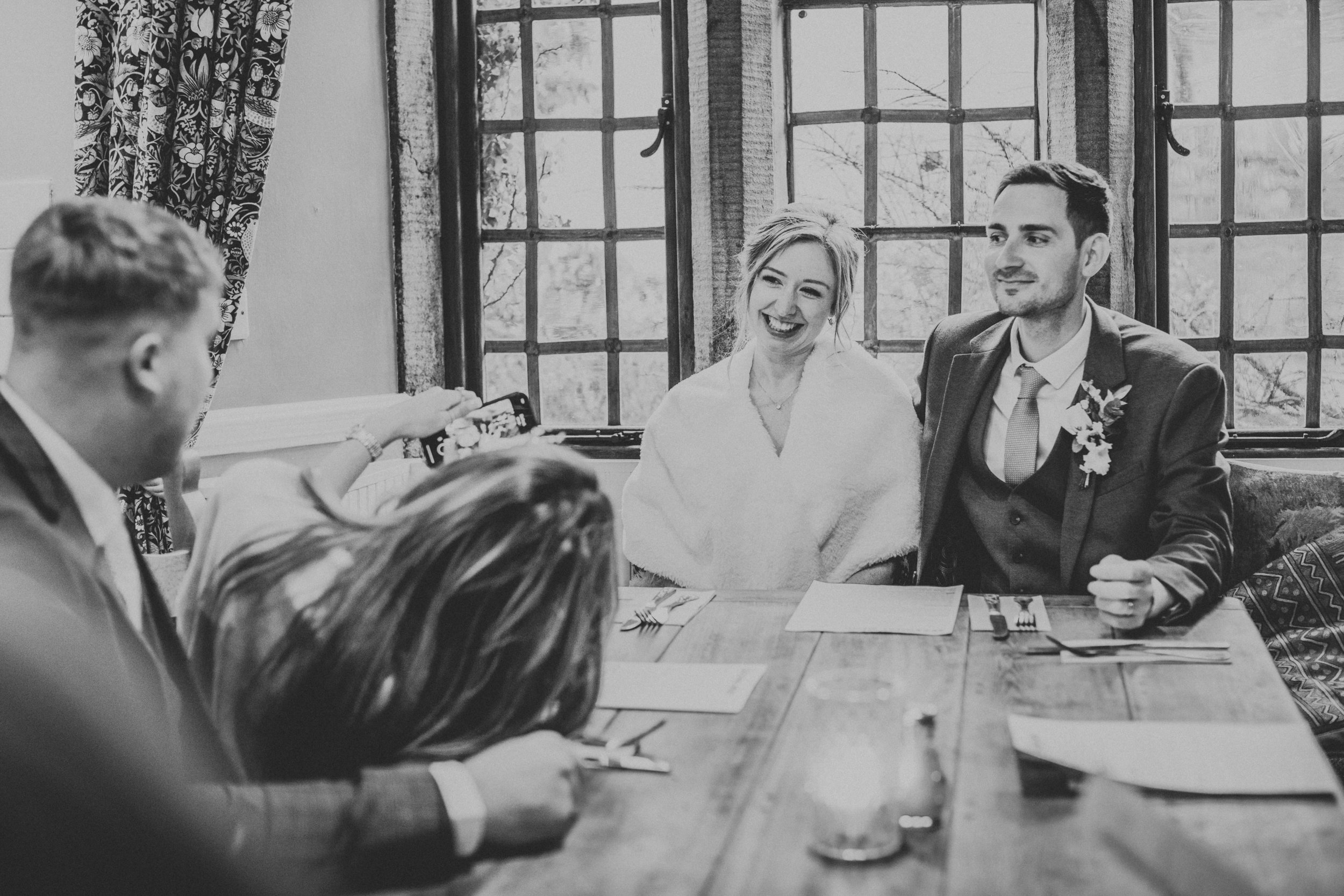 Black and white photo of Bride and Groom watching their wedding guests enjoy themselves. 