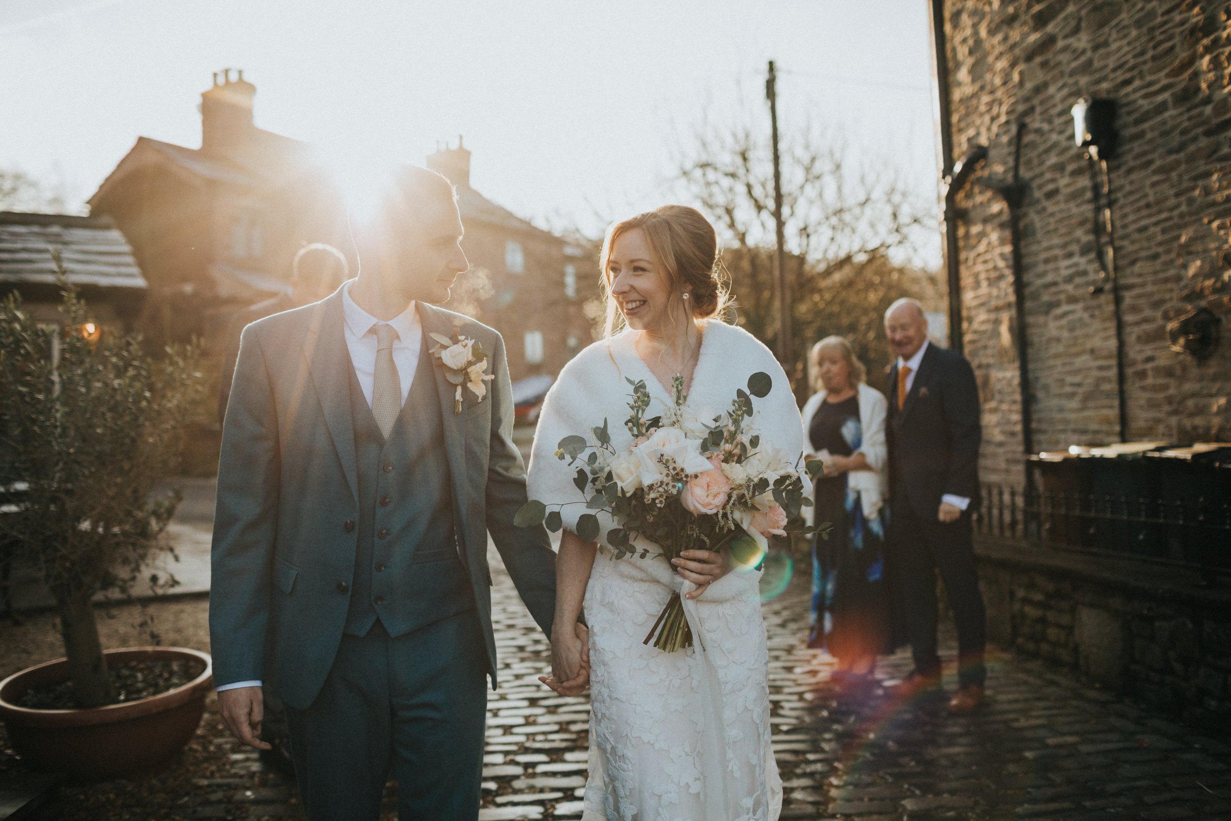 Bride and Groom walking along a cobbled street with the sun behind them. 