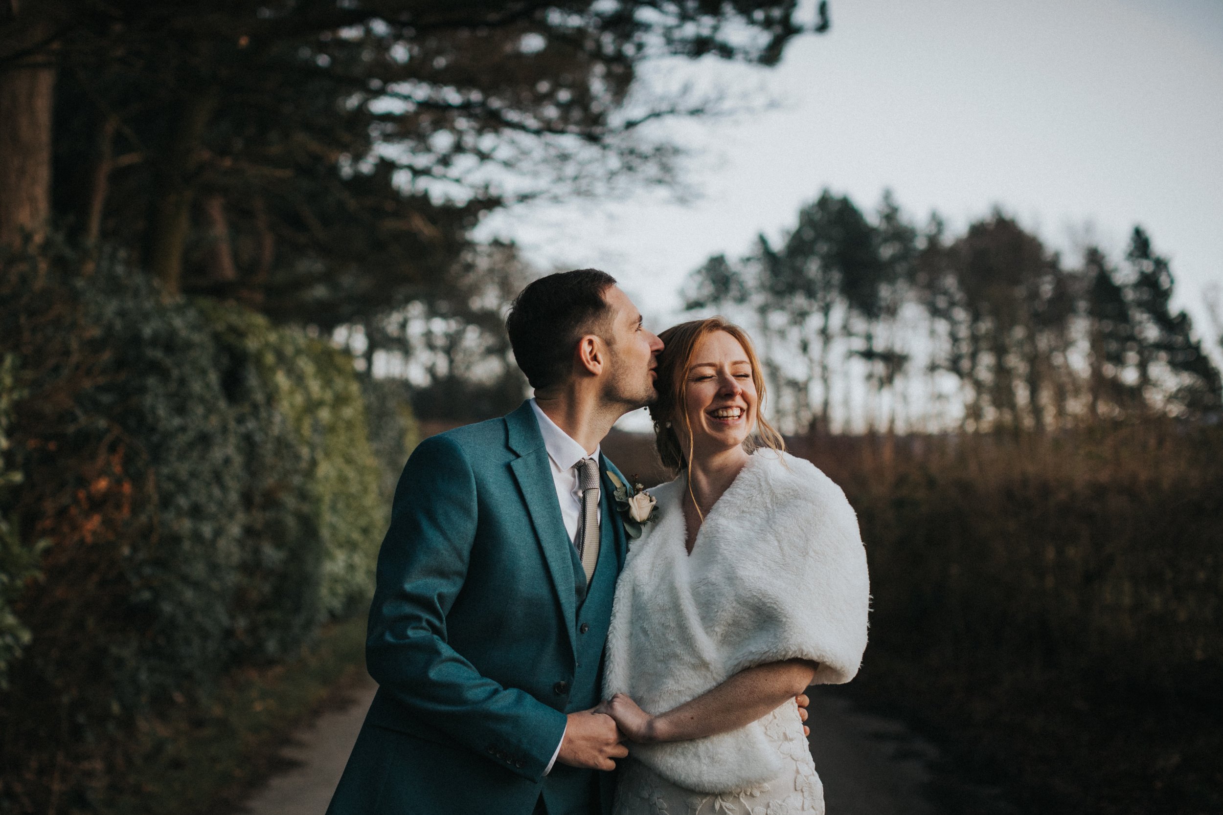 Groom gives his bride a kiss on the head as she laughs. 