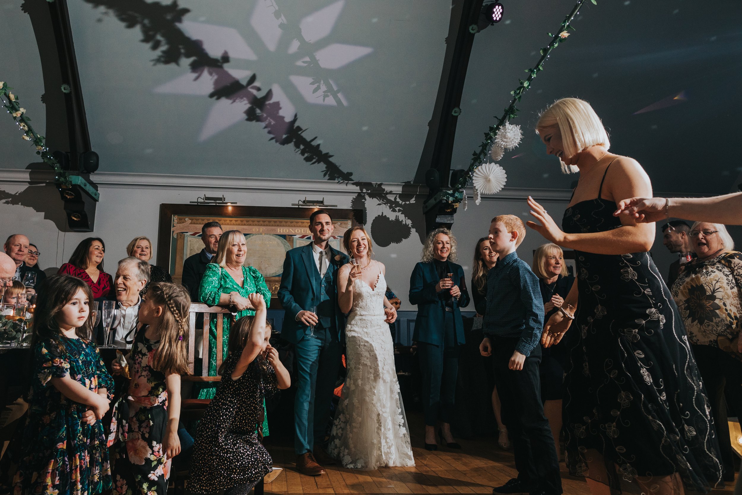 Bride and Groom laughing while children and guests dance in the foreground. 