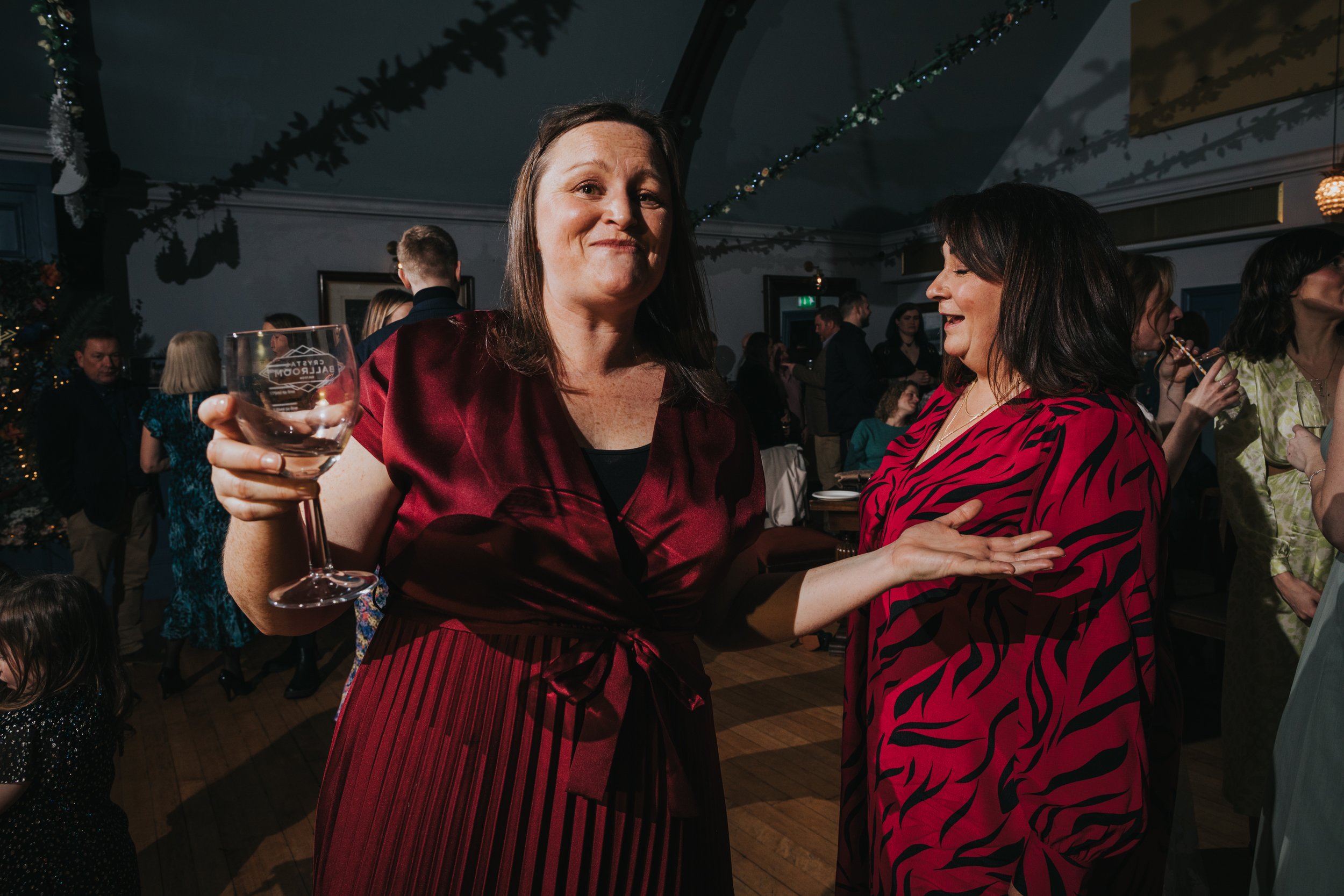 Wedding guest dancing with a drink in her hand wearing a red dress. 