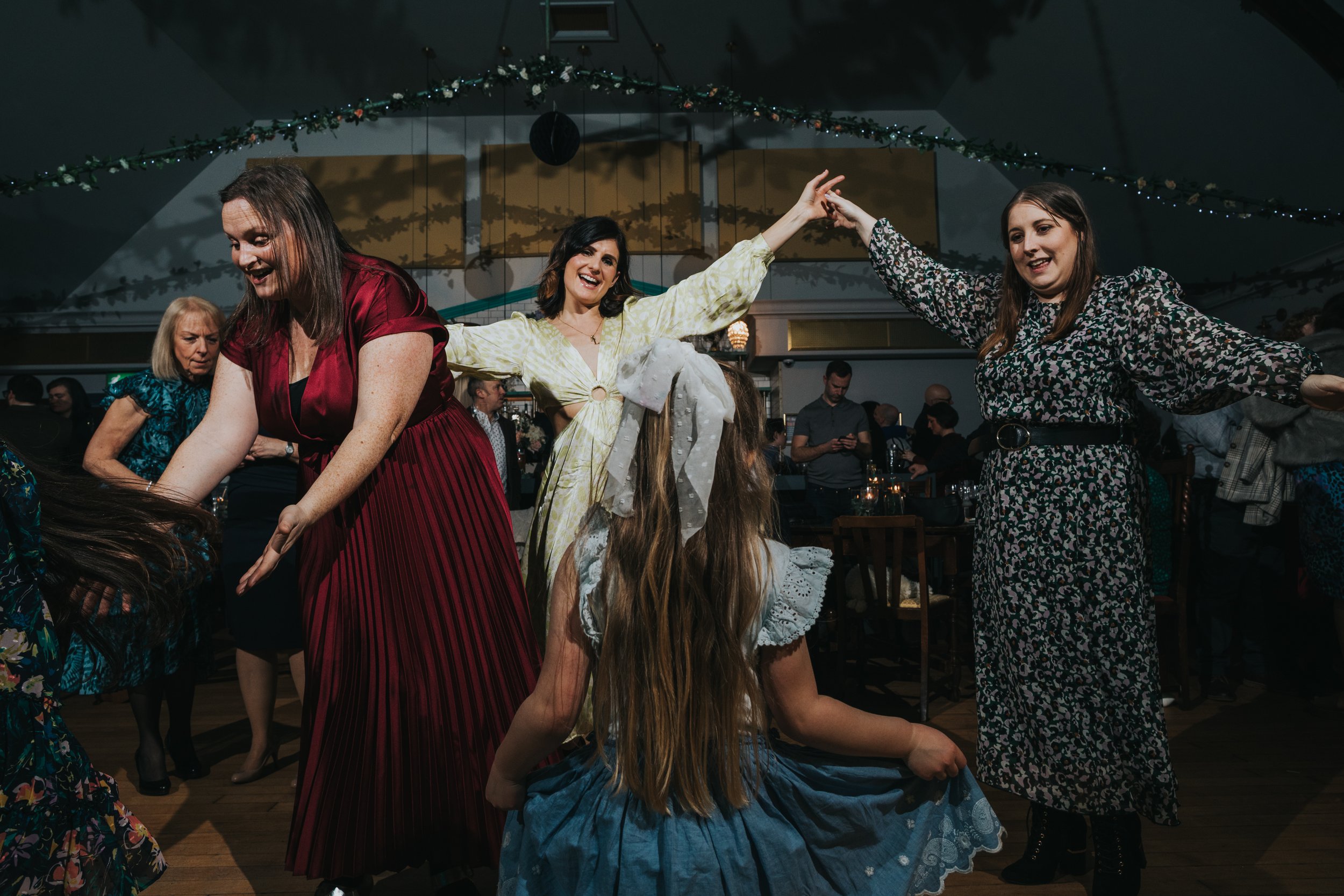 Female wedding guests dance with little girl in a blue dress.