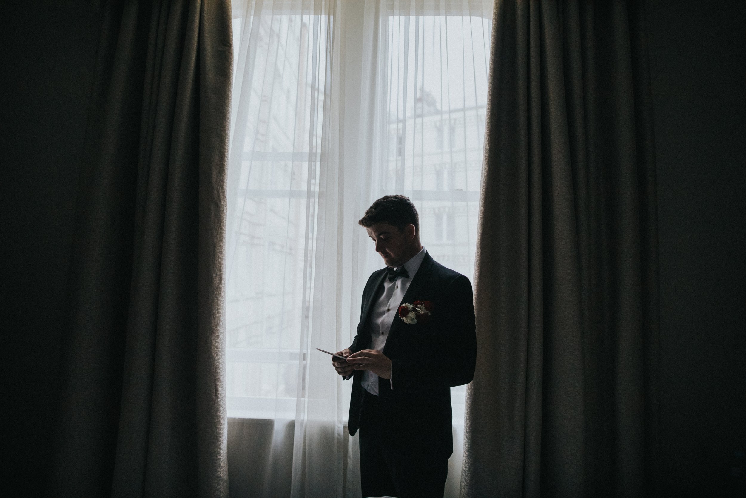 Groom reading a letter from his bride next to the window at the Midland Hotel Manchester.