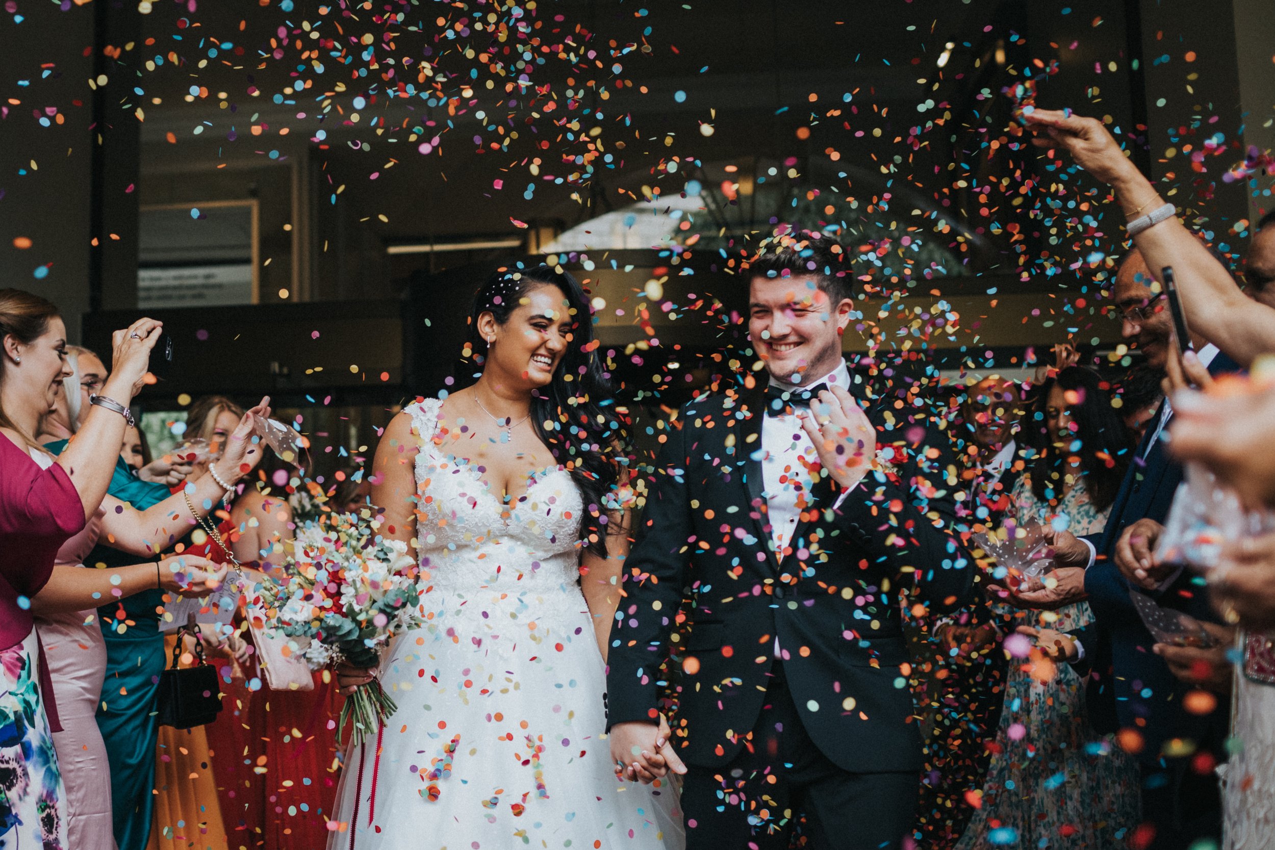 Bride and Groom laugh as confetti hits them in the face. 