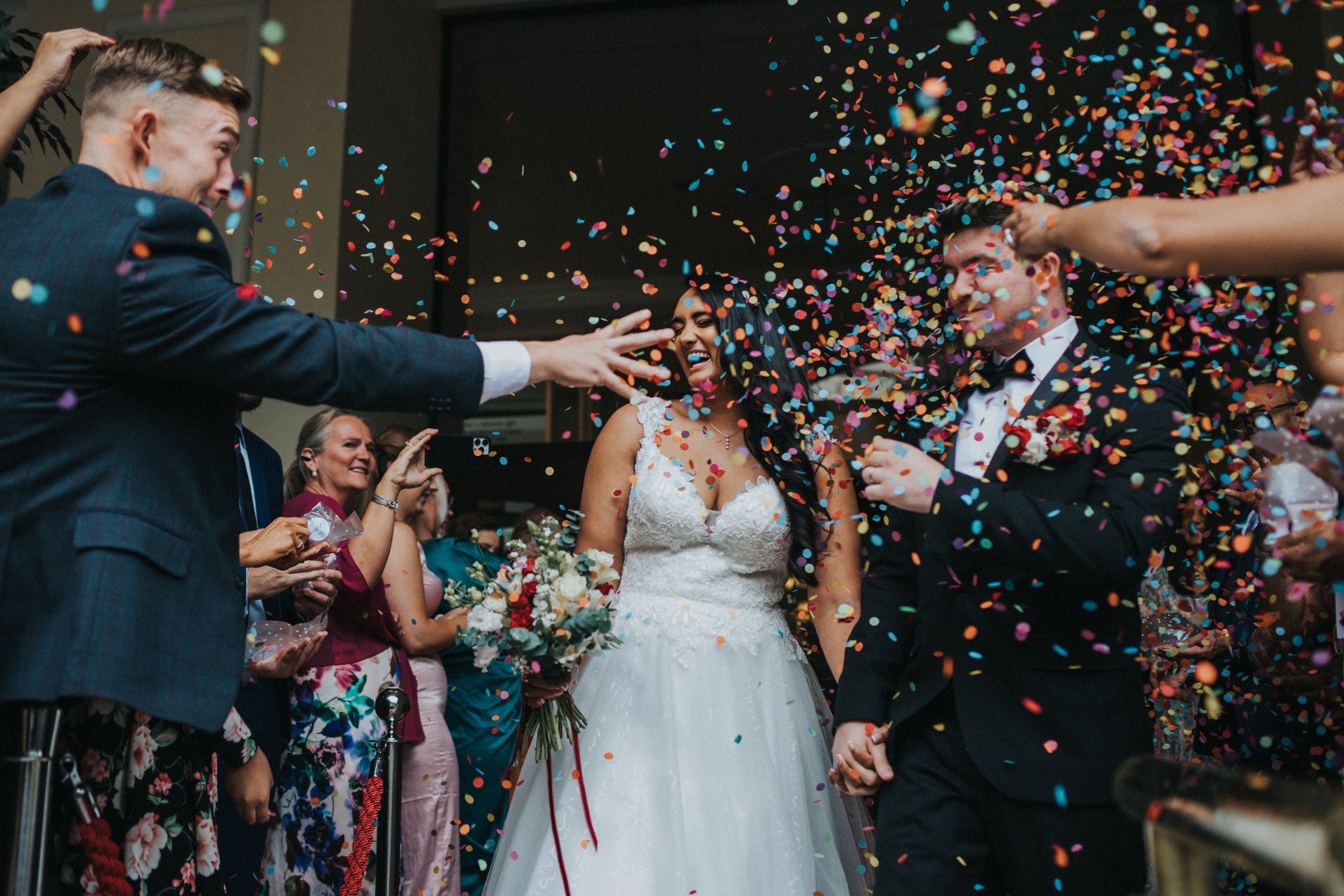 Wedding guests jumps at couple with a handful of confetti. 