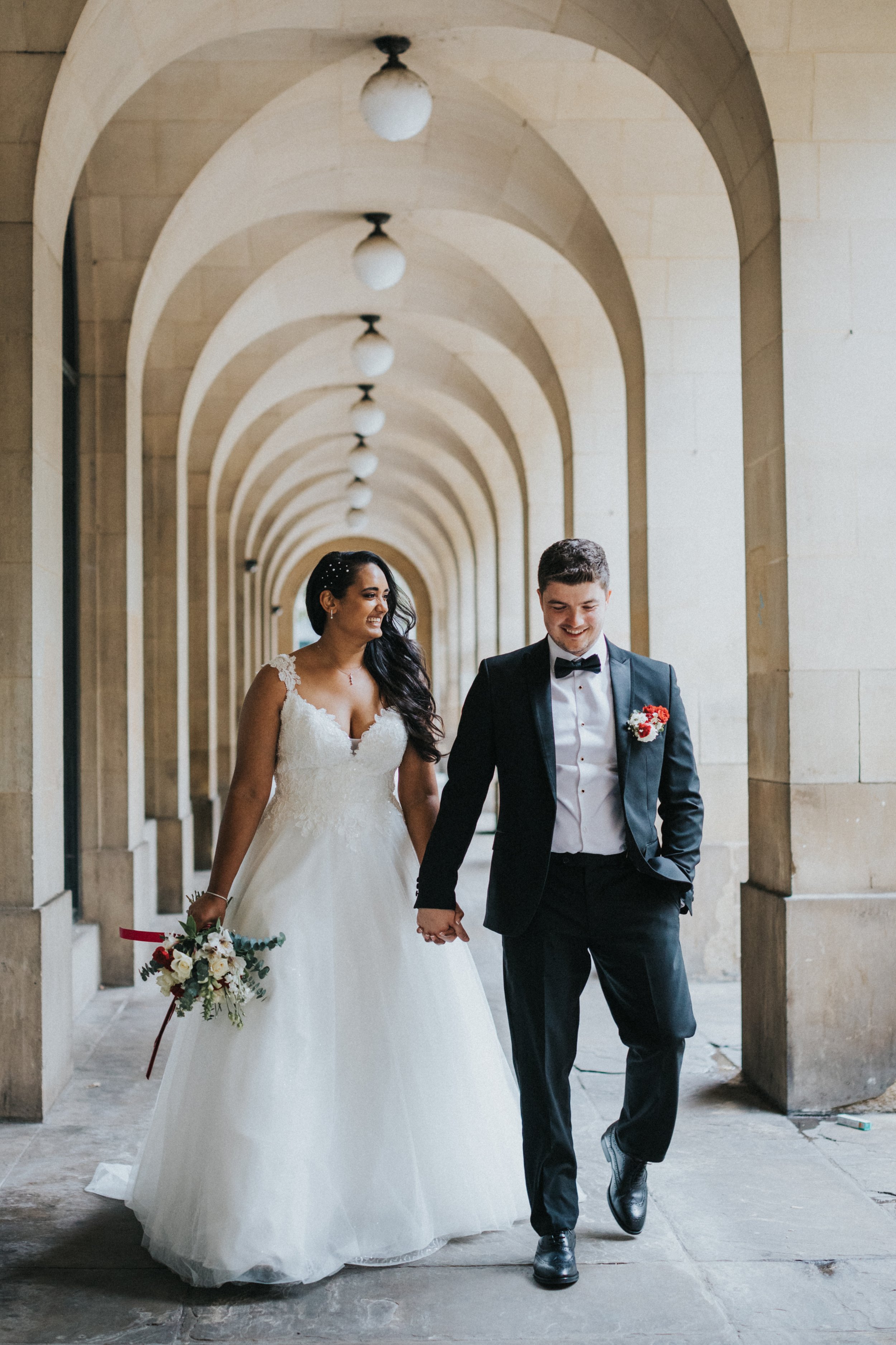 Bride and Groom walk under the arches together at Manchester Hall. 