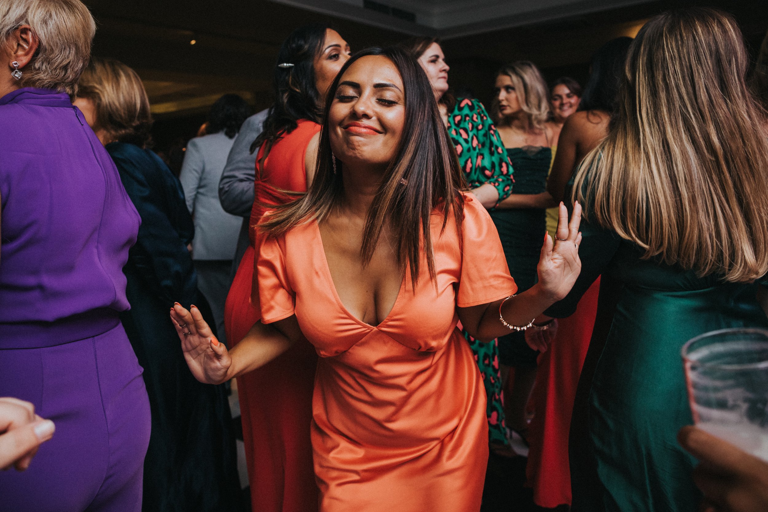 Woman in orange dress smiling and dancing with her eyes closed.