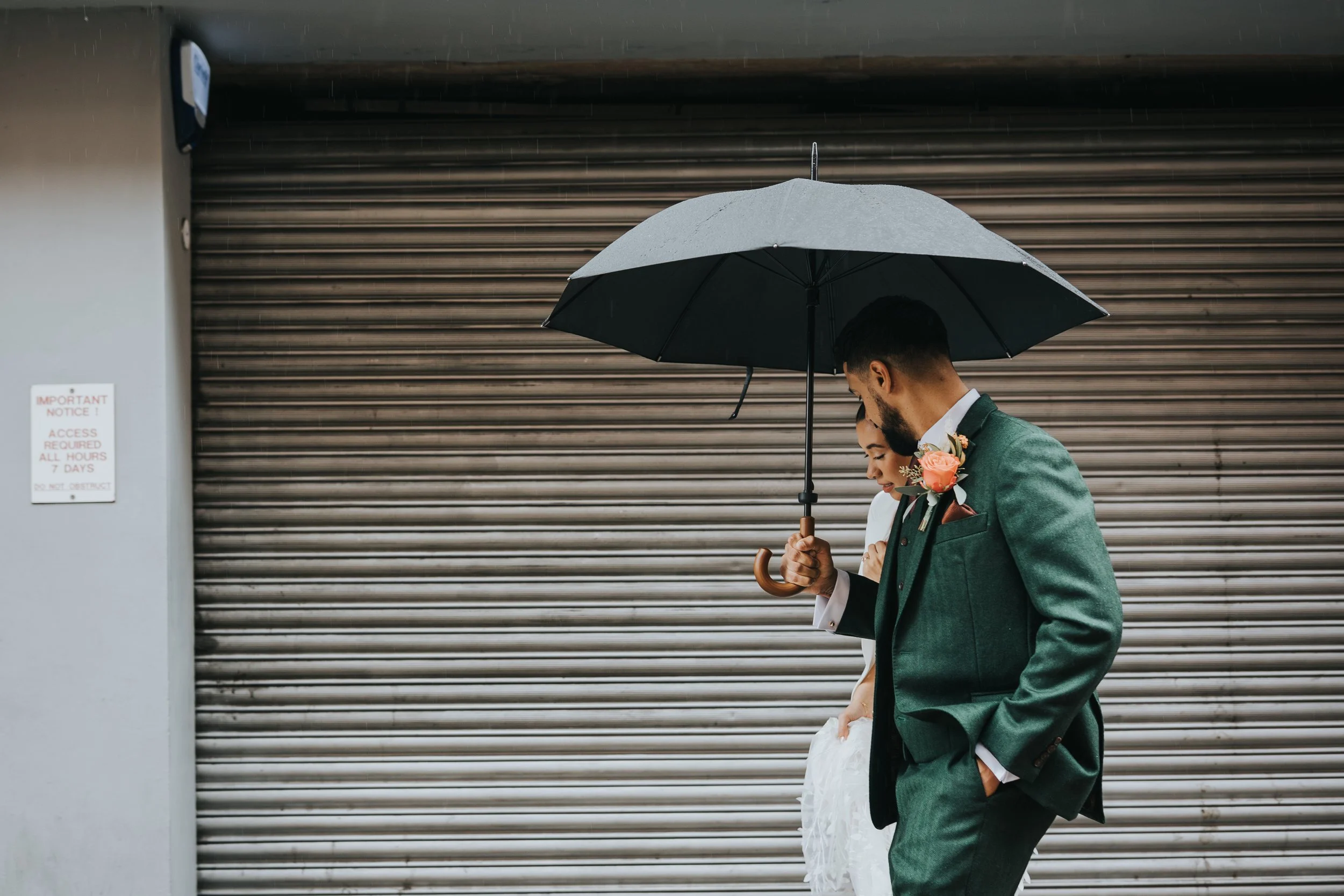 Bride and groom under an umbrella infront of a shutter door