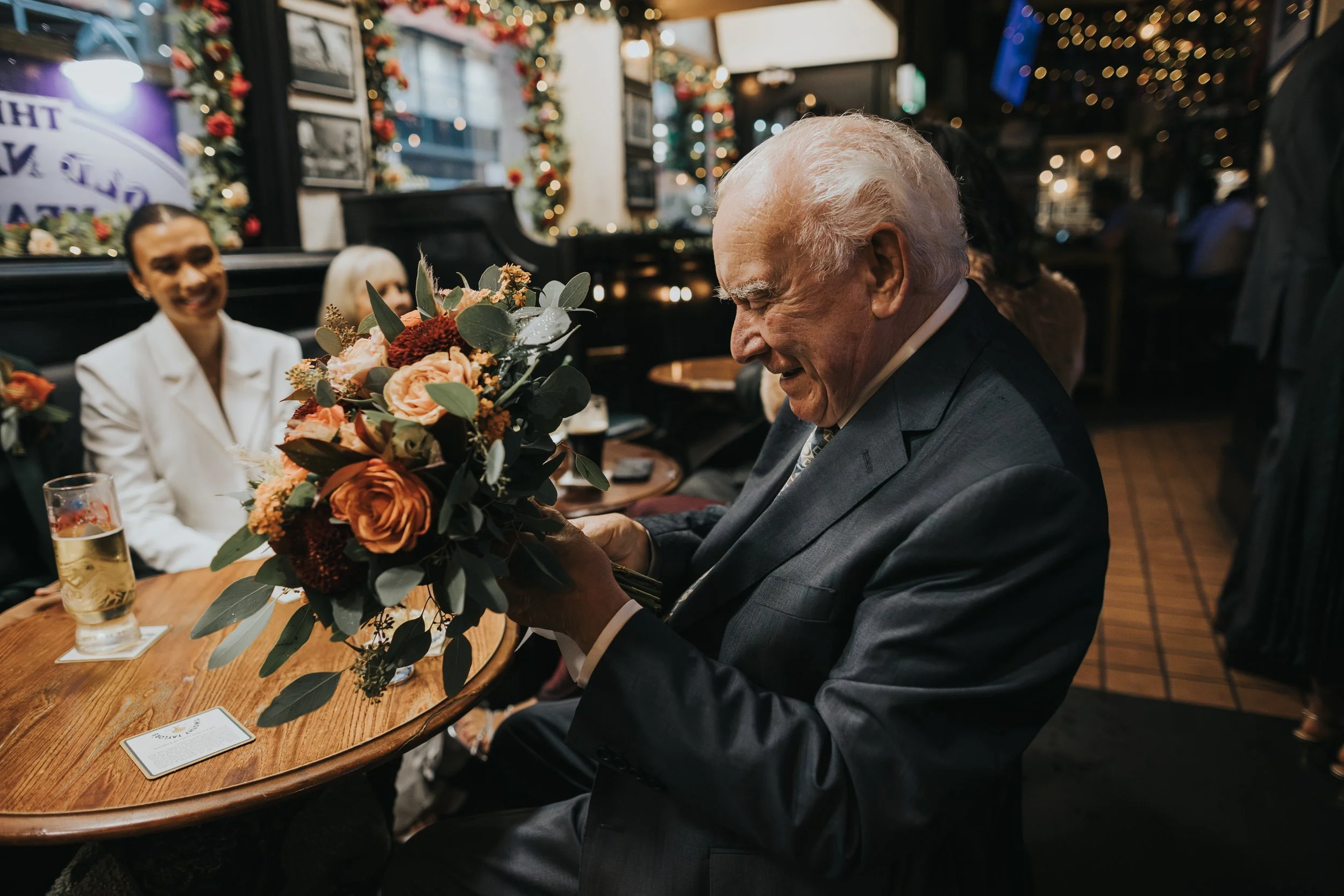 Grandad looking at photograph attached to brides bouquet. 