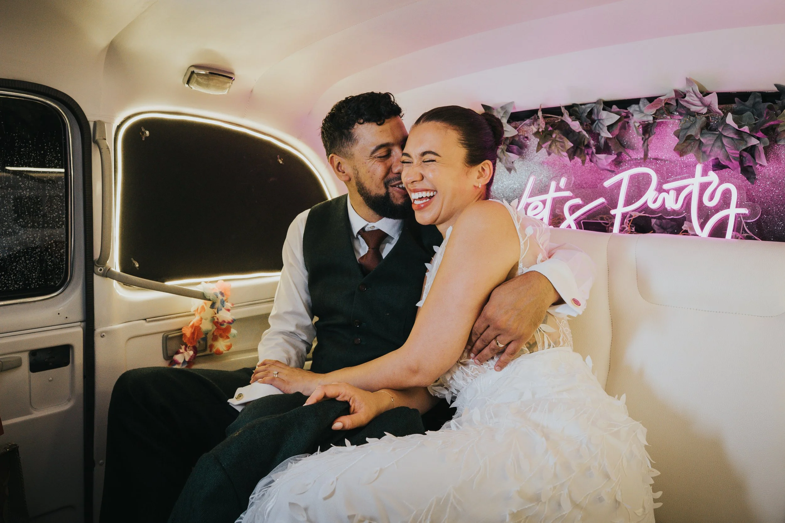 Bride and Groom in taxi photobooth with "lets party" neon sign behind them