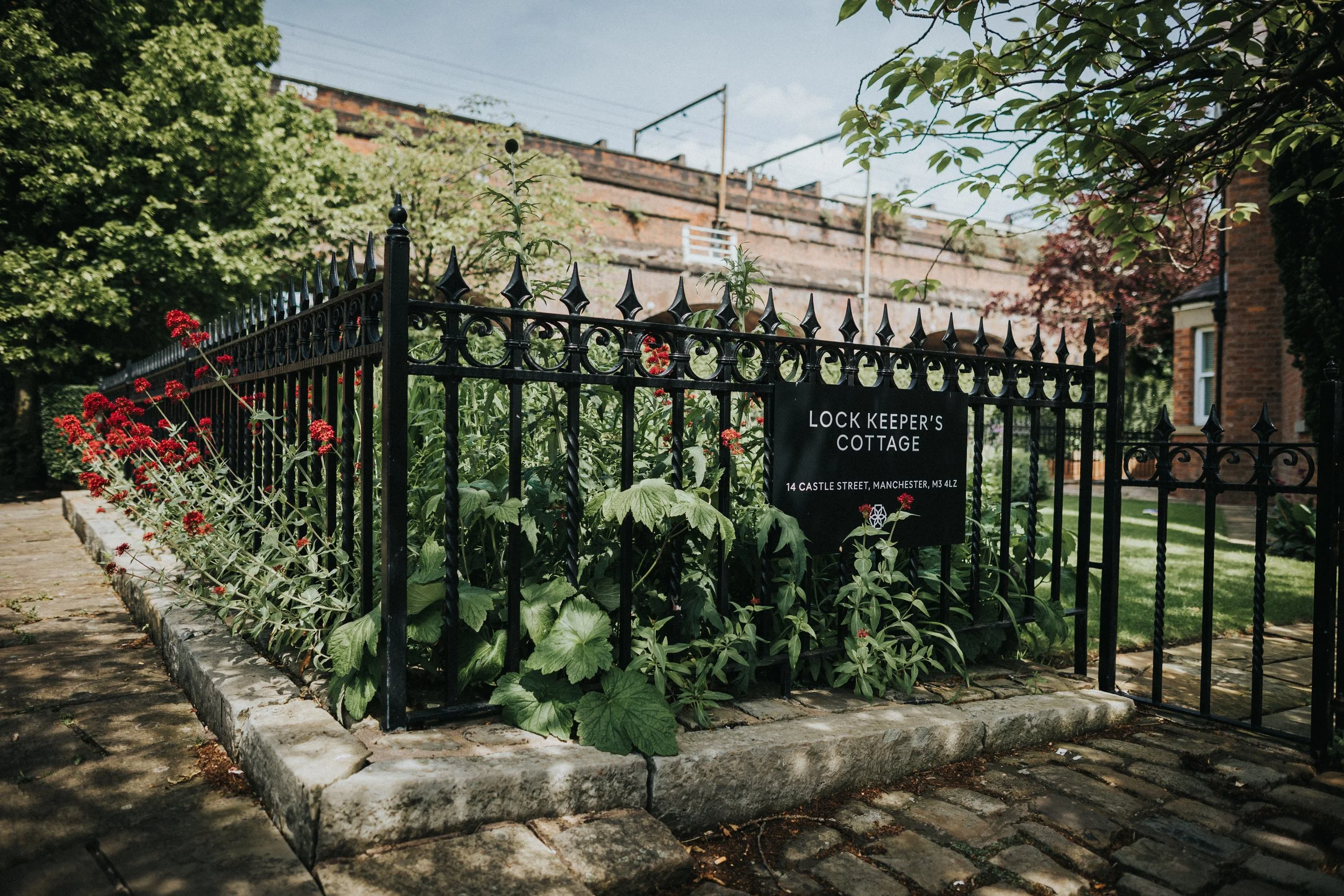 The iron fence and sign for The Lock Keepers Cottage and wild flowers. 