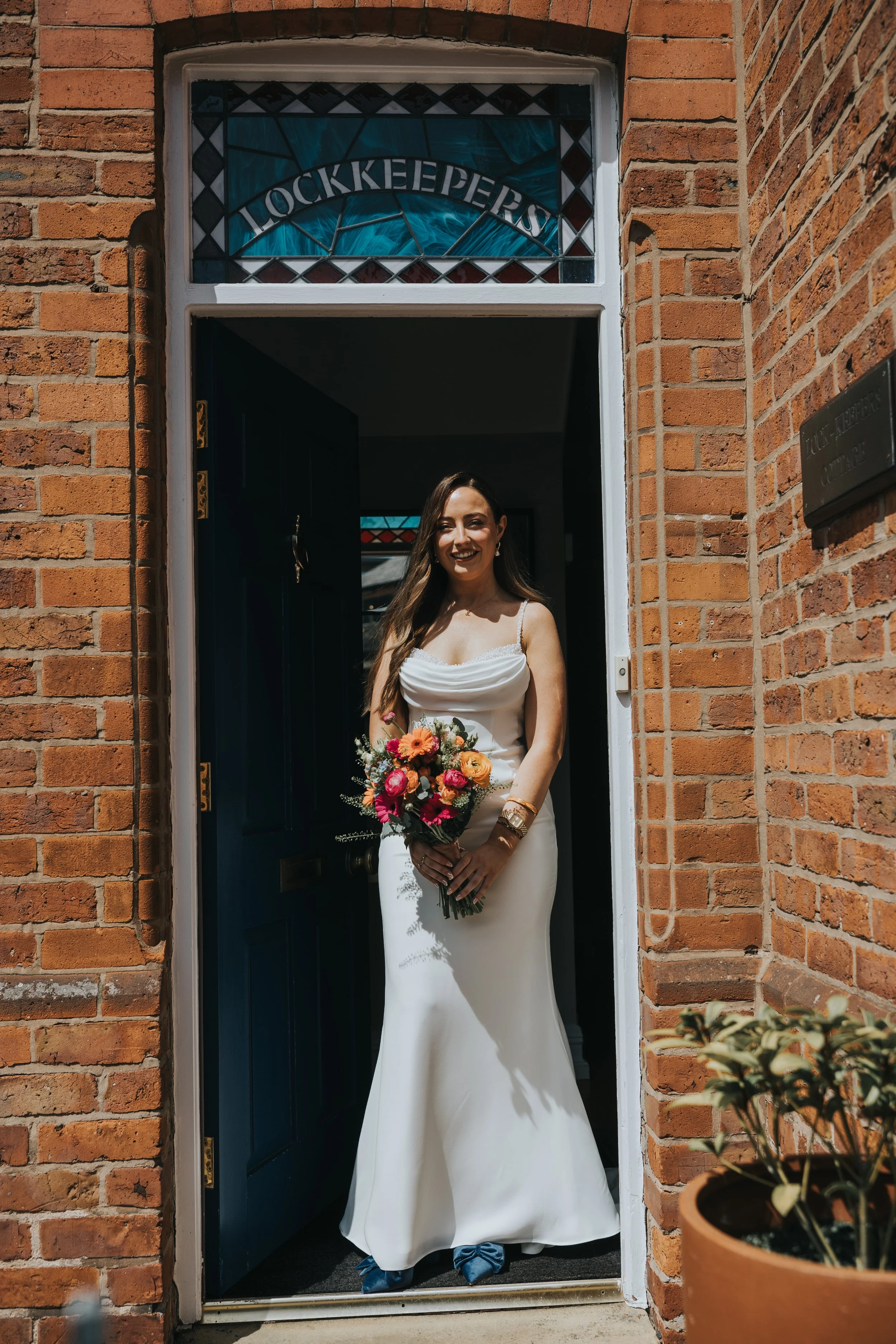 Bride at the door of the lock keepers cottage holding her wedding bouquet. 