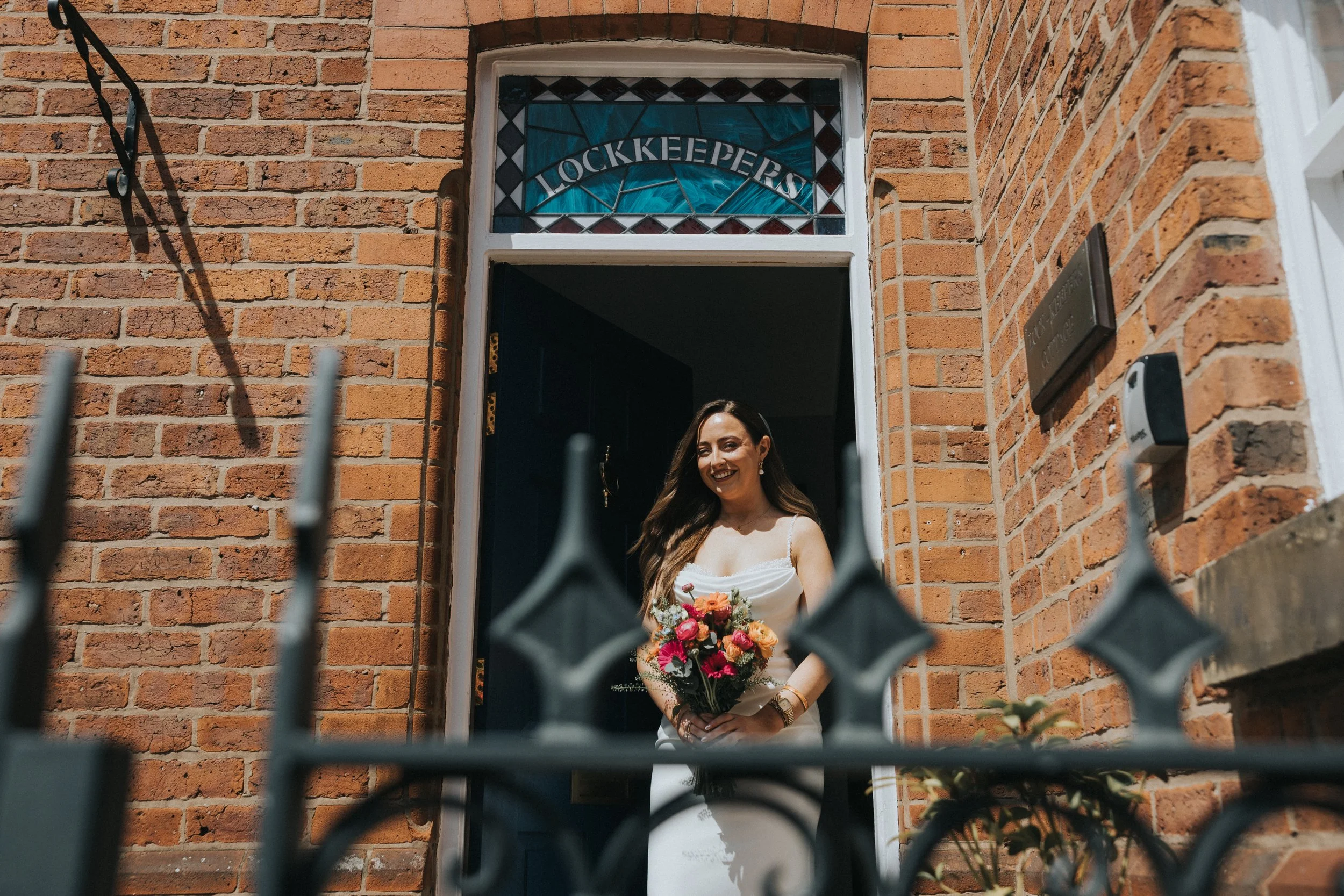 Bride at the door of the lock keepers cottage photographer through iron railings. 
