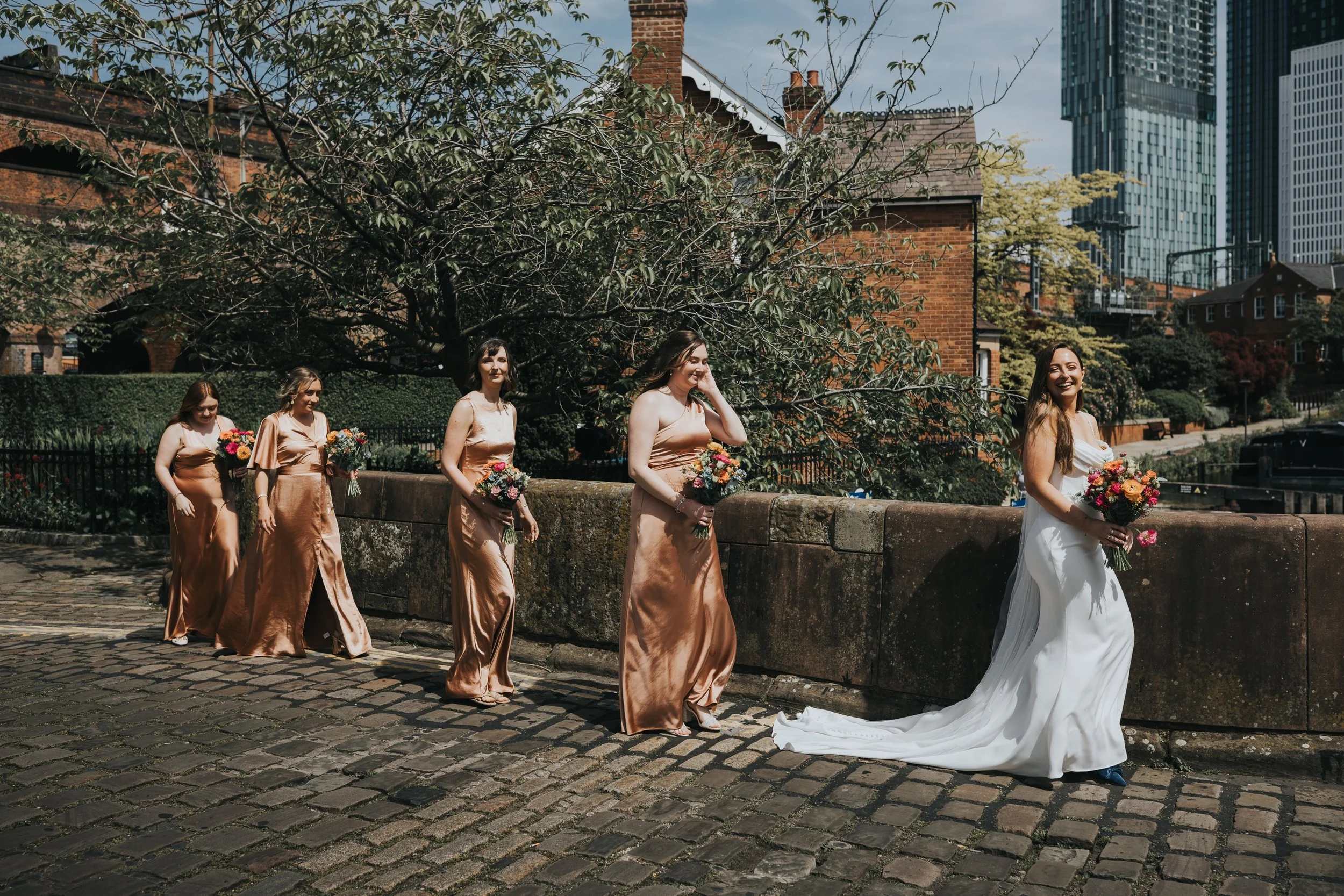 Bride leading her bridesmaids across canal bridge in Castlefield. 