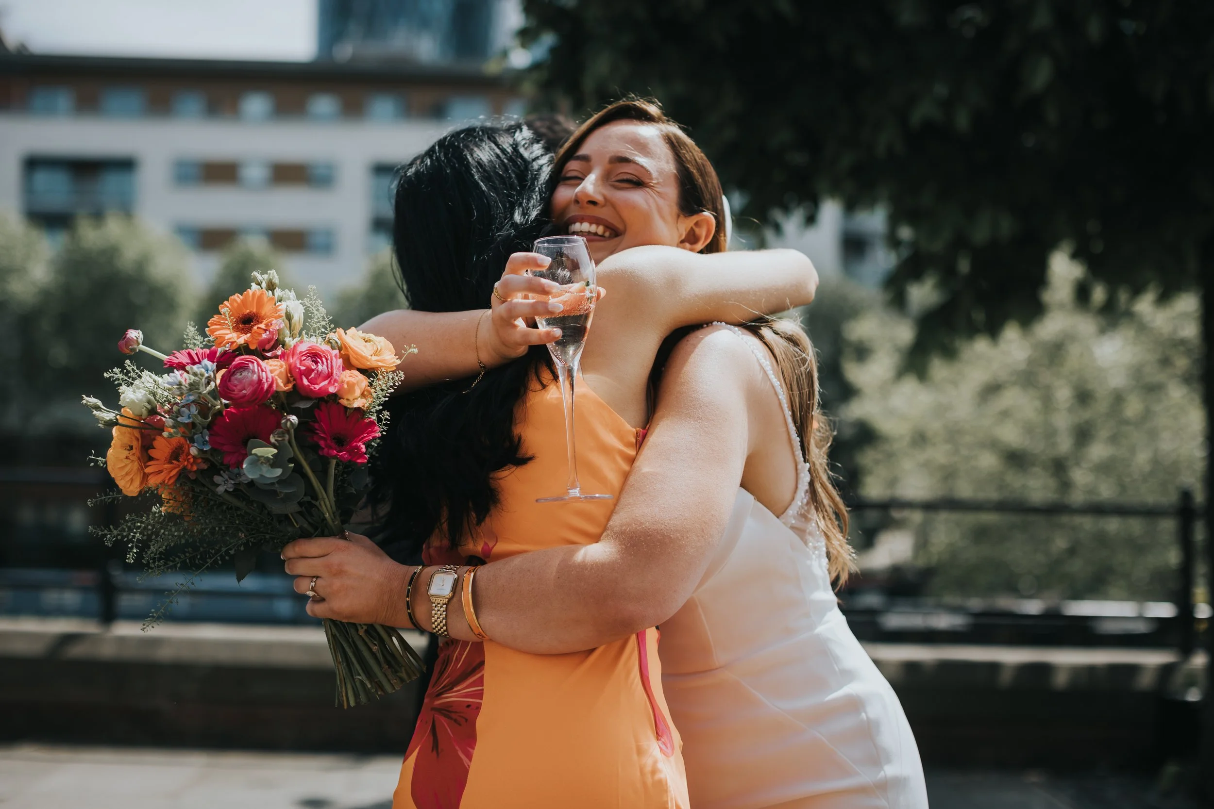 Bride hugs guest wearing bright orange dress. 
